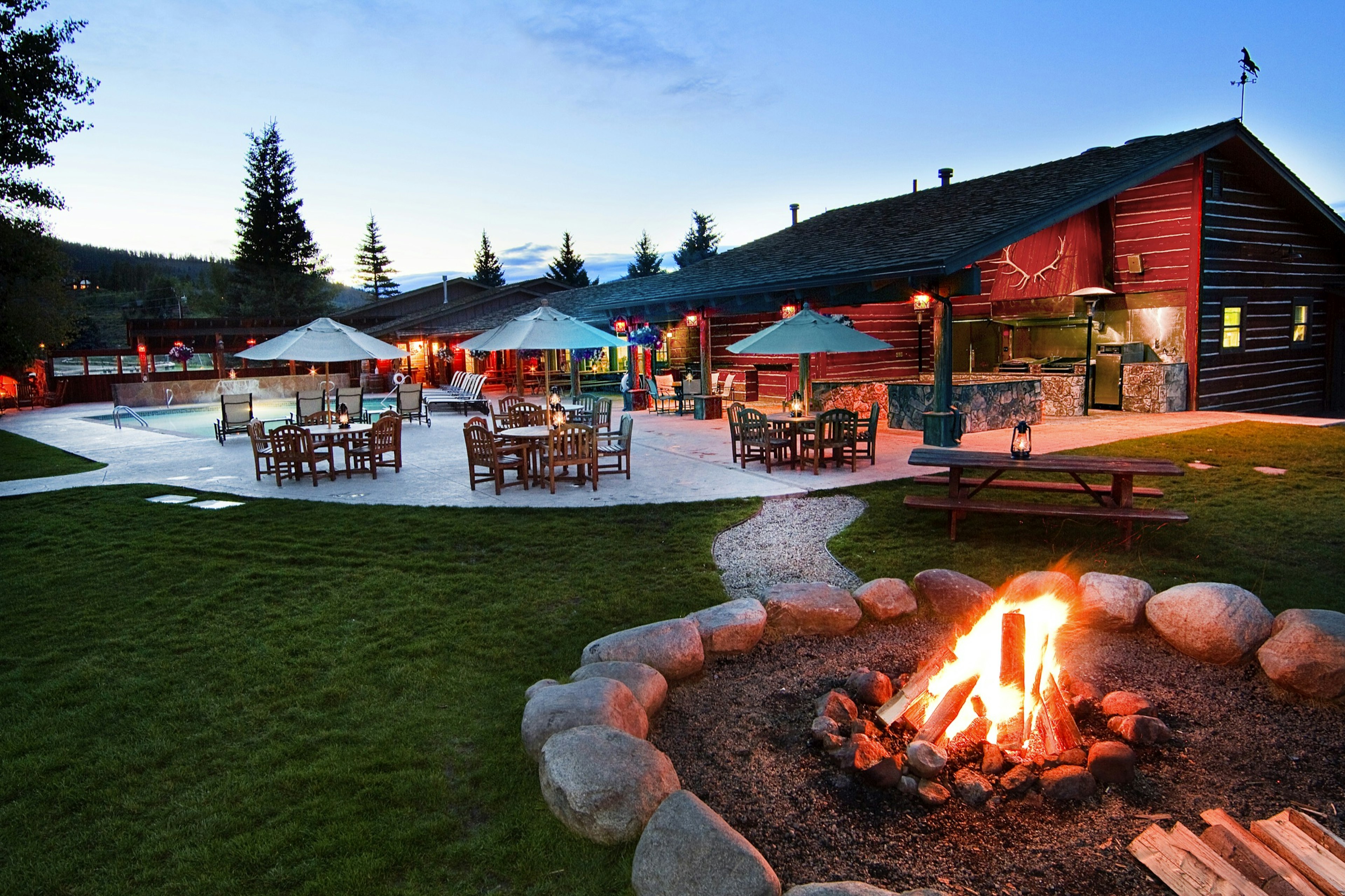 A fire rages in a fire pit around a landscaped patio with rustic western furniture at C Lazy U Ranch. 2019 is the 100th birthday anniversary of the guest dude ranch