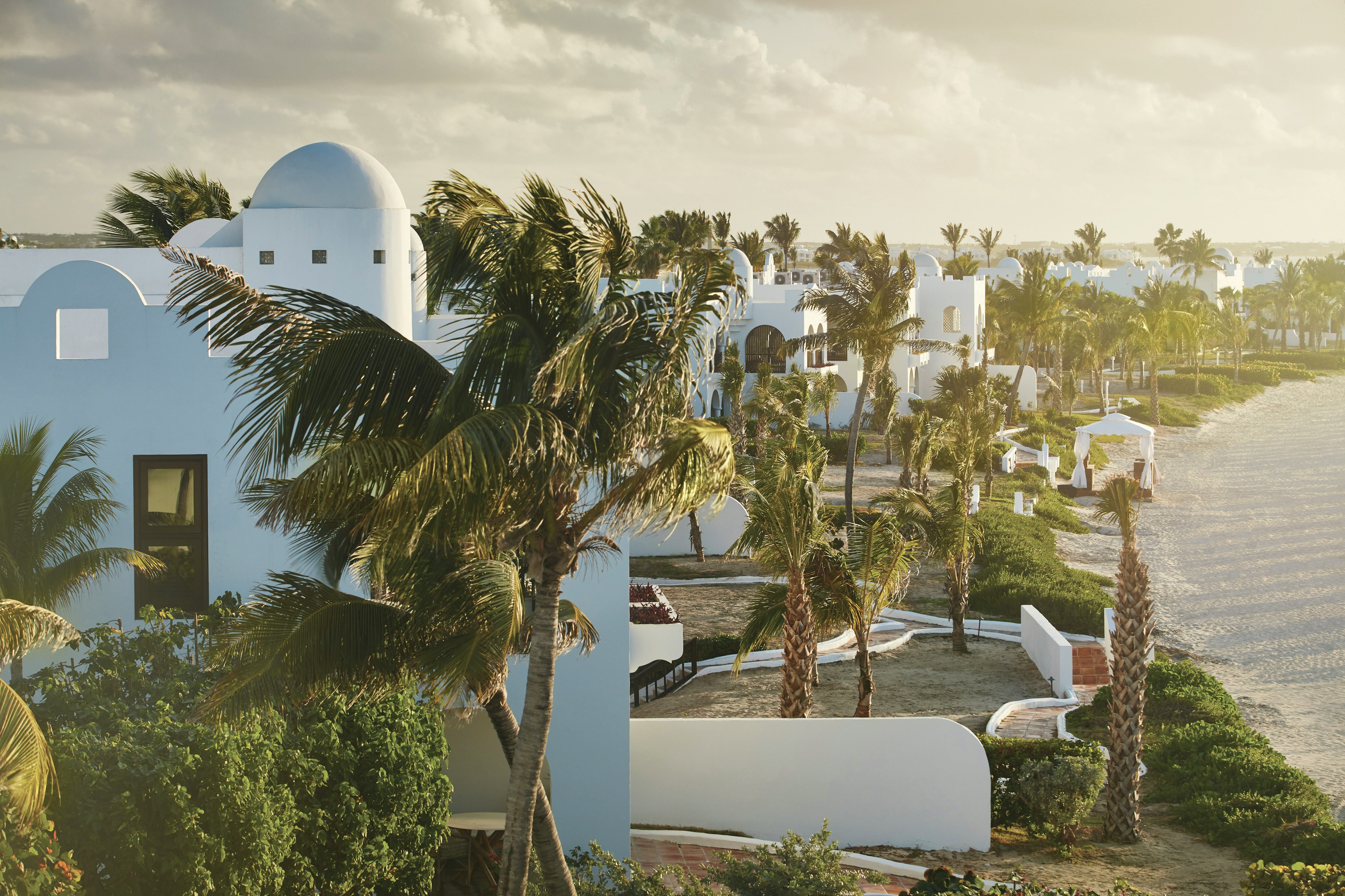 Private villas at the Belmond Cap Juluca along the beach. Palm trees are lined up alongside the villas.