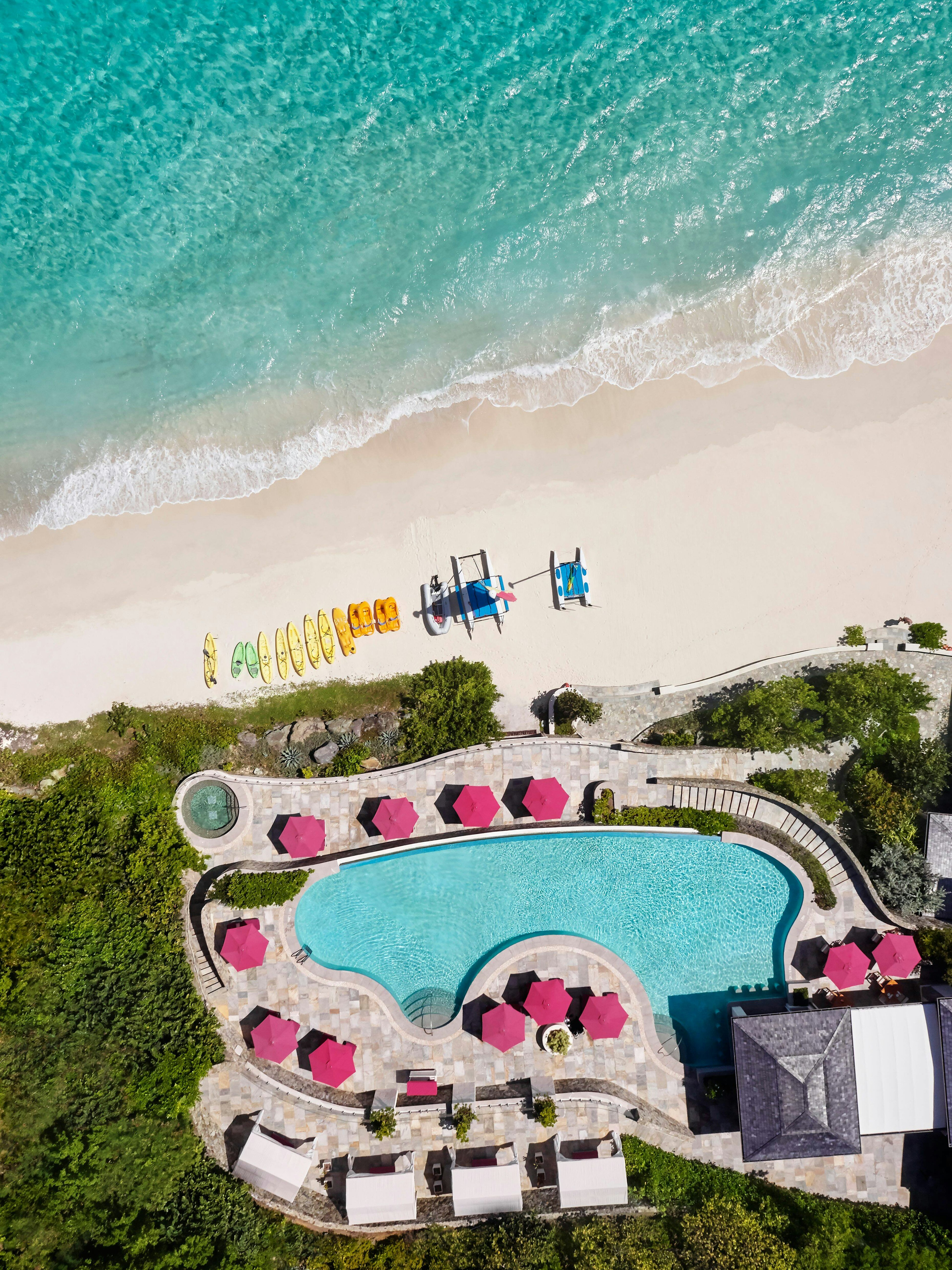 An aerial shot of the pool at the Mandarin Oriental, St Vincent and the Grenadines. Pink parasols are around the side of the pool.