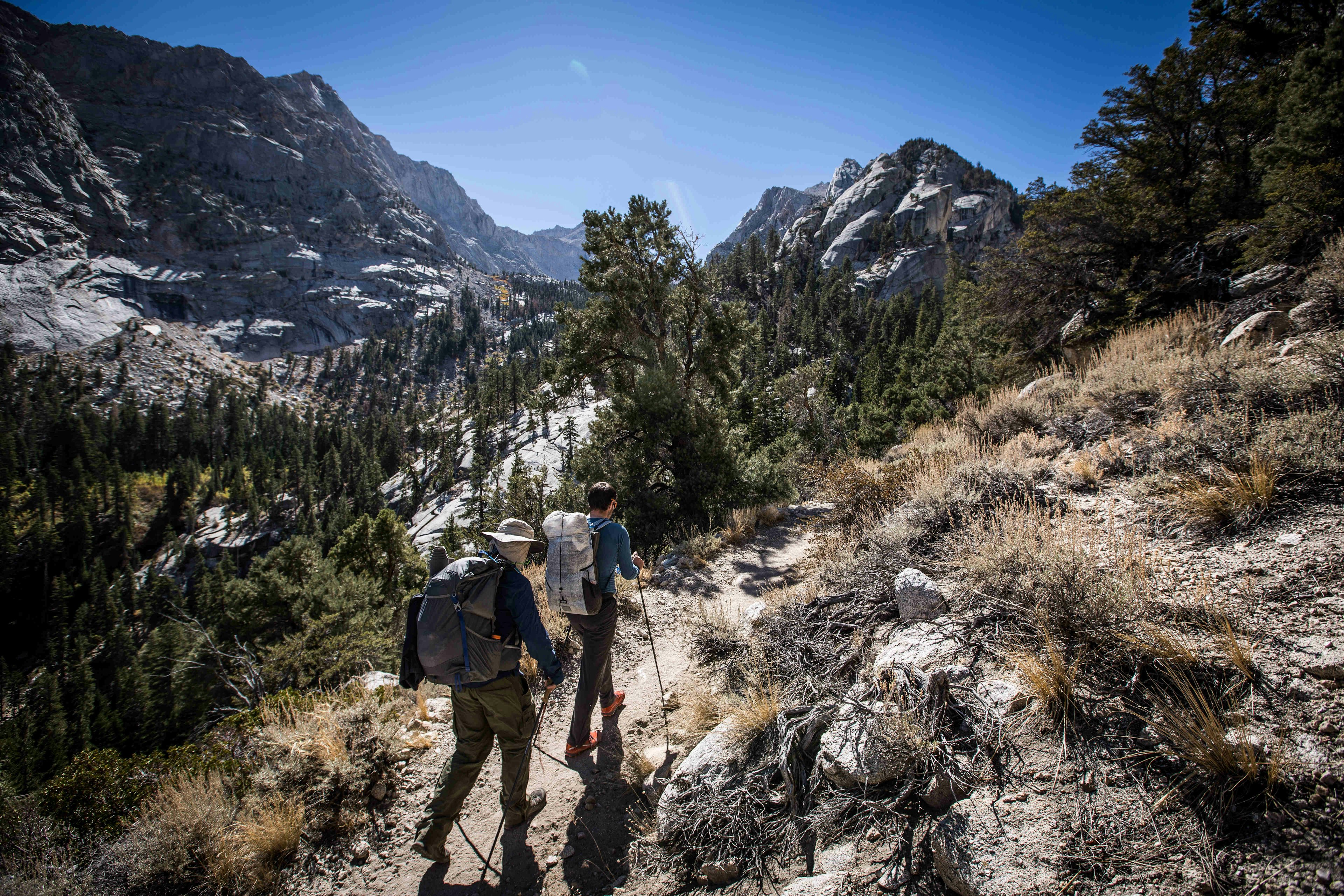 Two hikers with backpacks and poles ascend Mt Whitney in California with snow-capped mountains all around