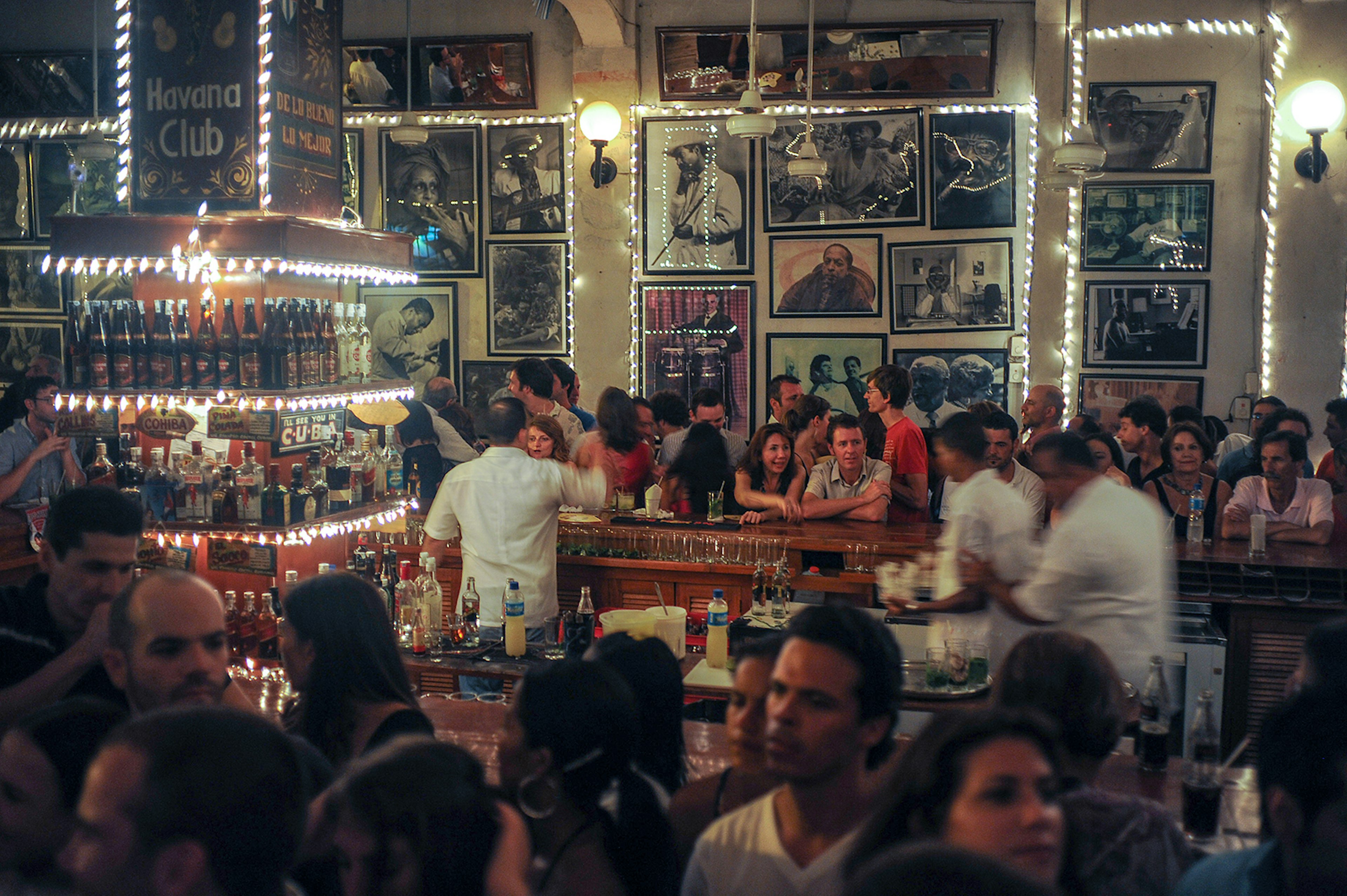 A crowd stands around a central bar decorated with strings of lights and Cuban-inspired art © Kaveh Kazemi / Getty Images