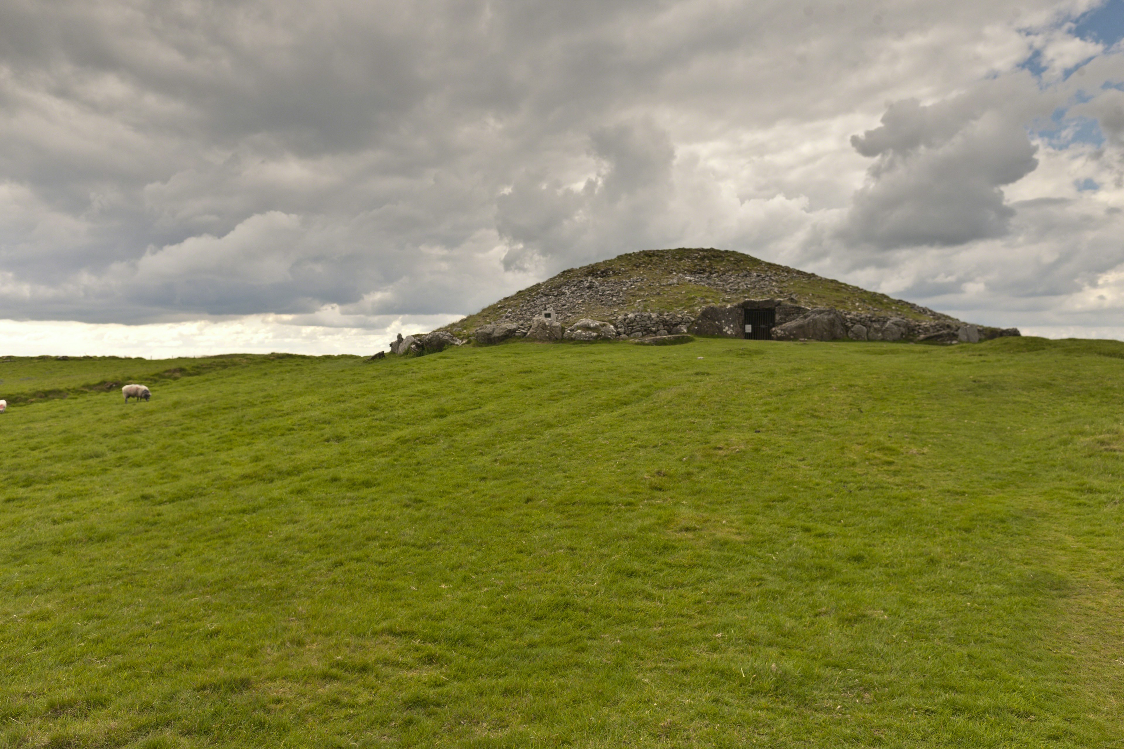 A large stone tomb sits atop a green hilltop in Loughcrew Ireland