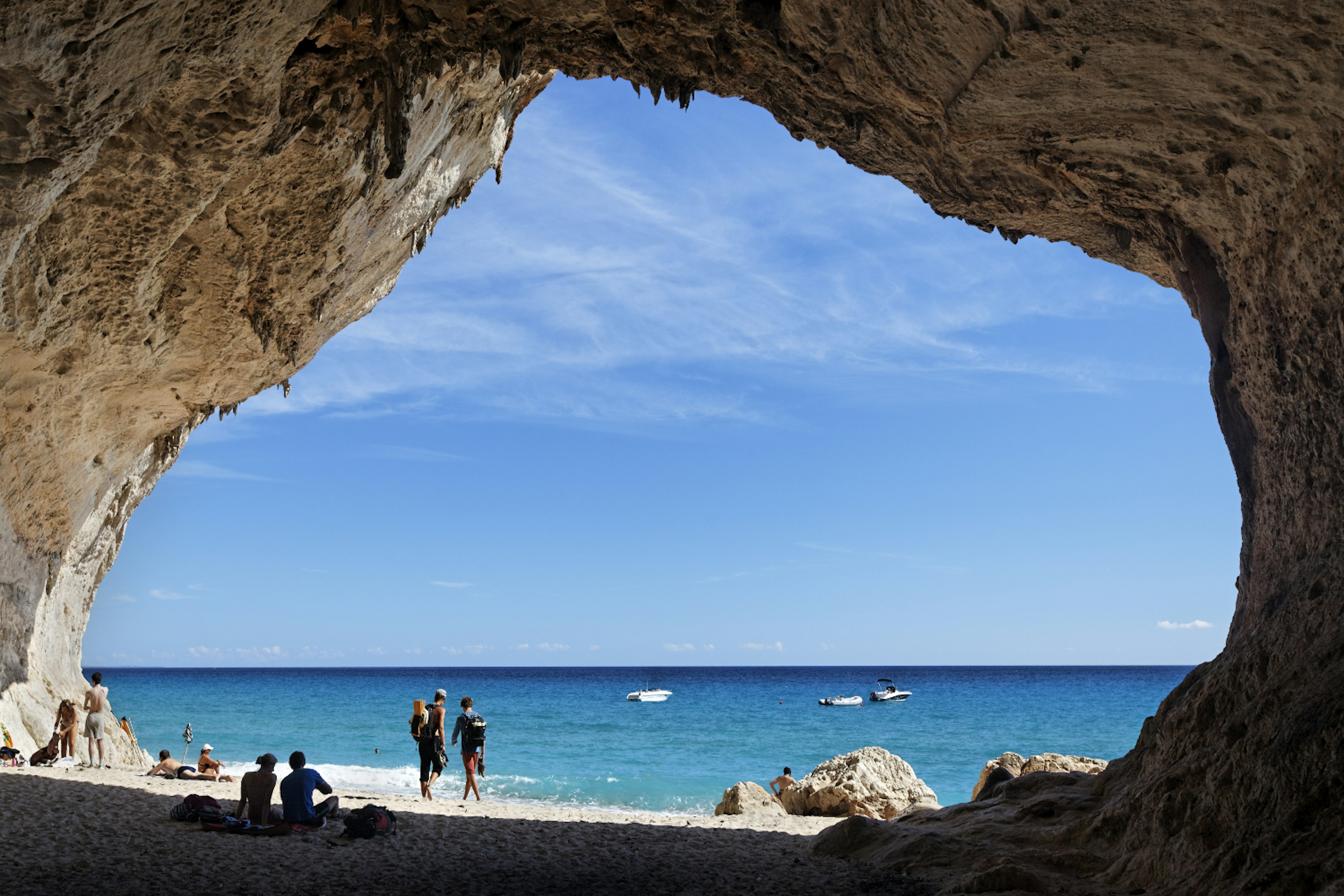 A group of people relax outside a cave on Cala Luna at Golfo di Orosei, Sardinia.