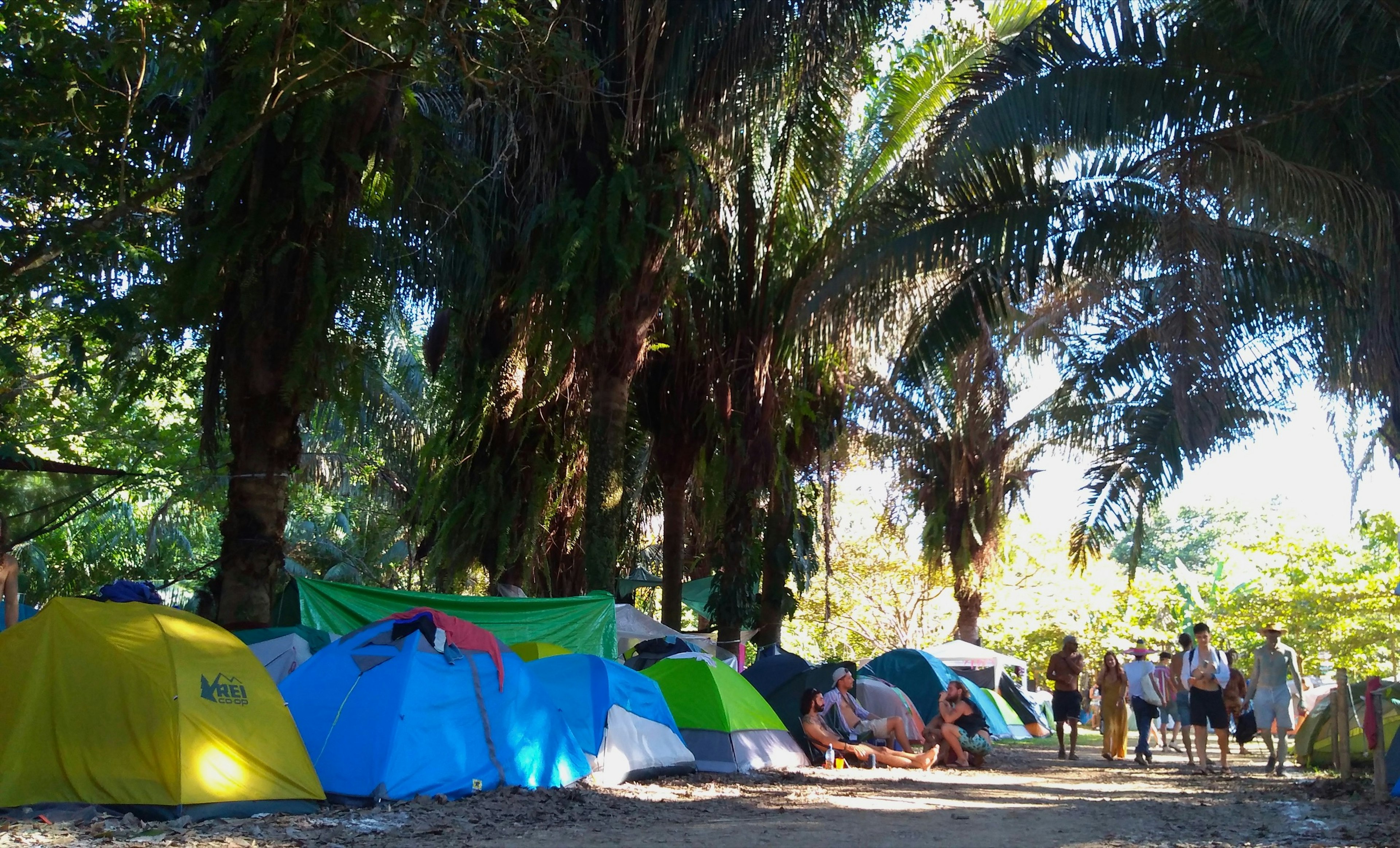 People walk under the tree canopy next to a line of colored tents at the Envision Festival in Costa Rica