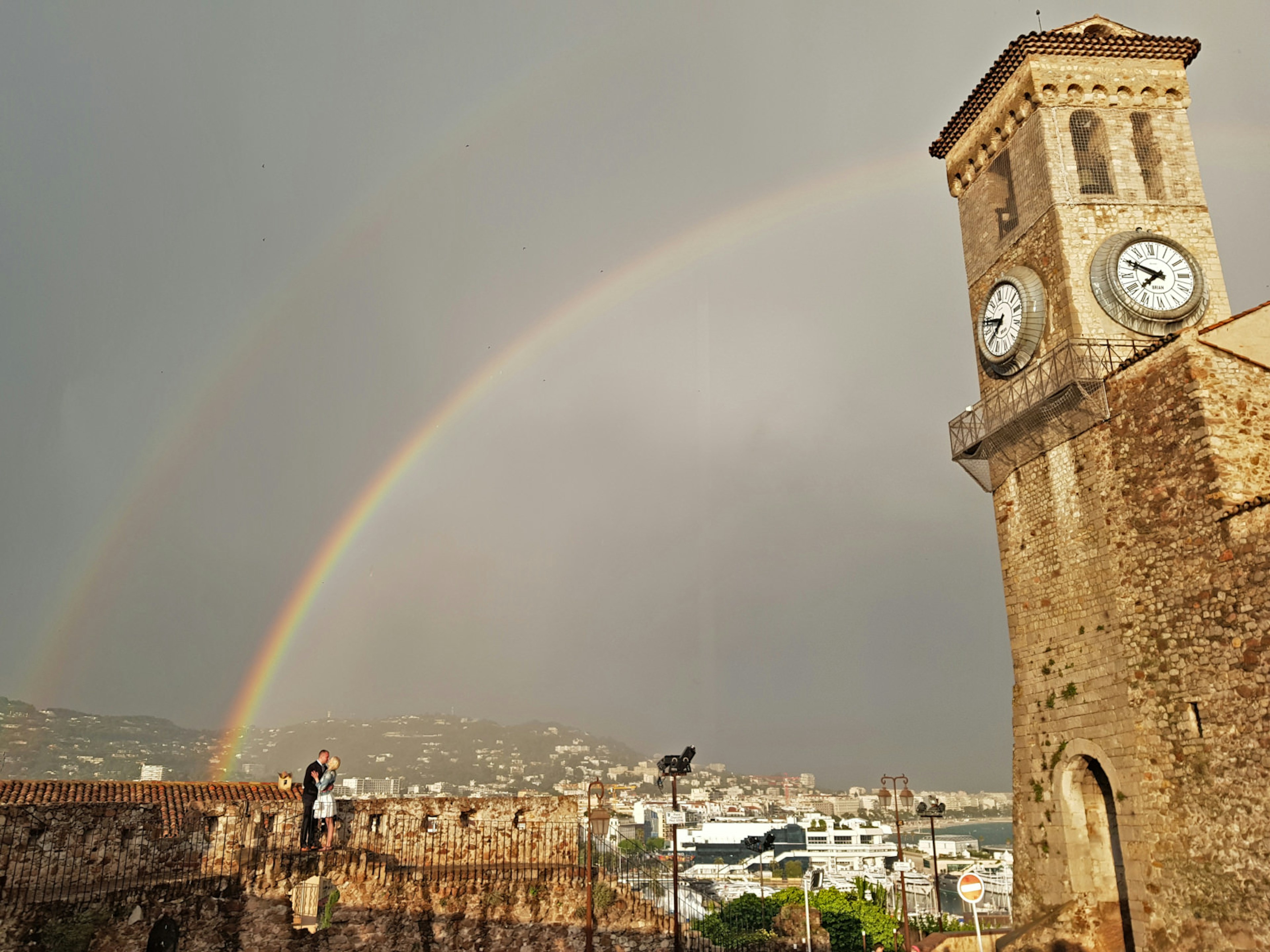 A couple kiss at Cannes castle whilst a rainbow beams across the sky in the background