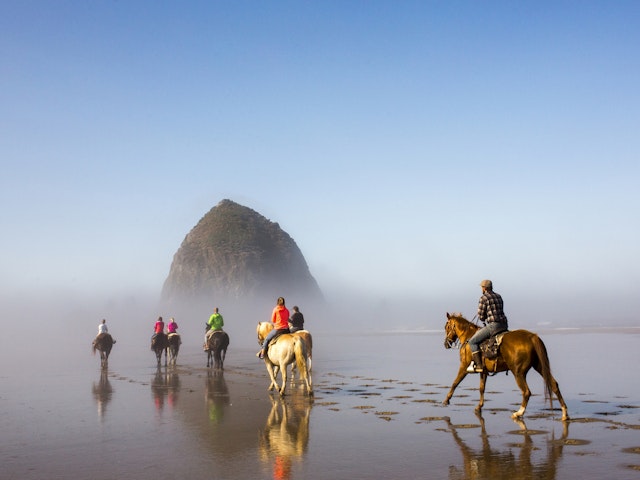 A group of people horseback riding along a beach through the misty conditions
