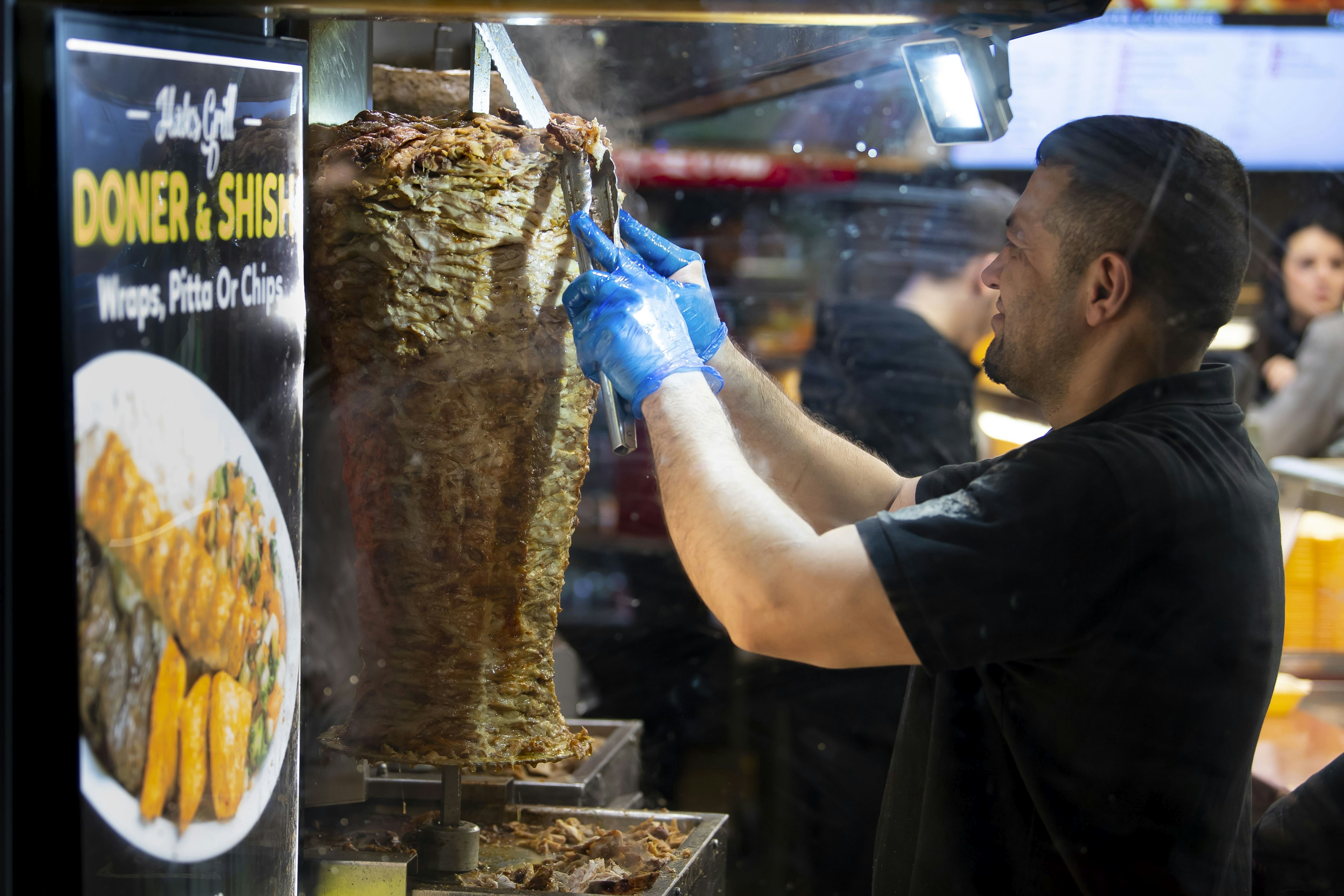 A chip shop worker sheers meat from a rotating stump of donner meat at an establishment on Caroline Street, Cardiff.