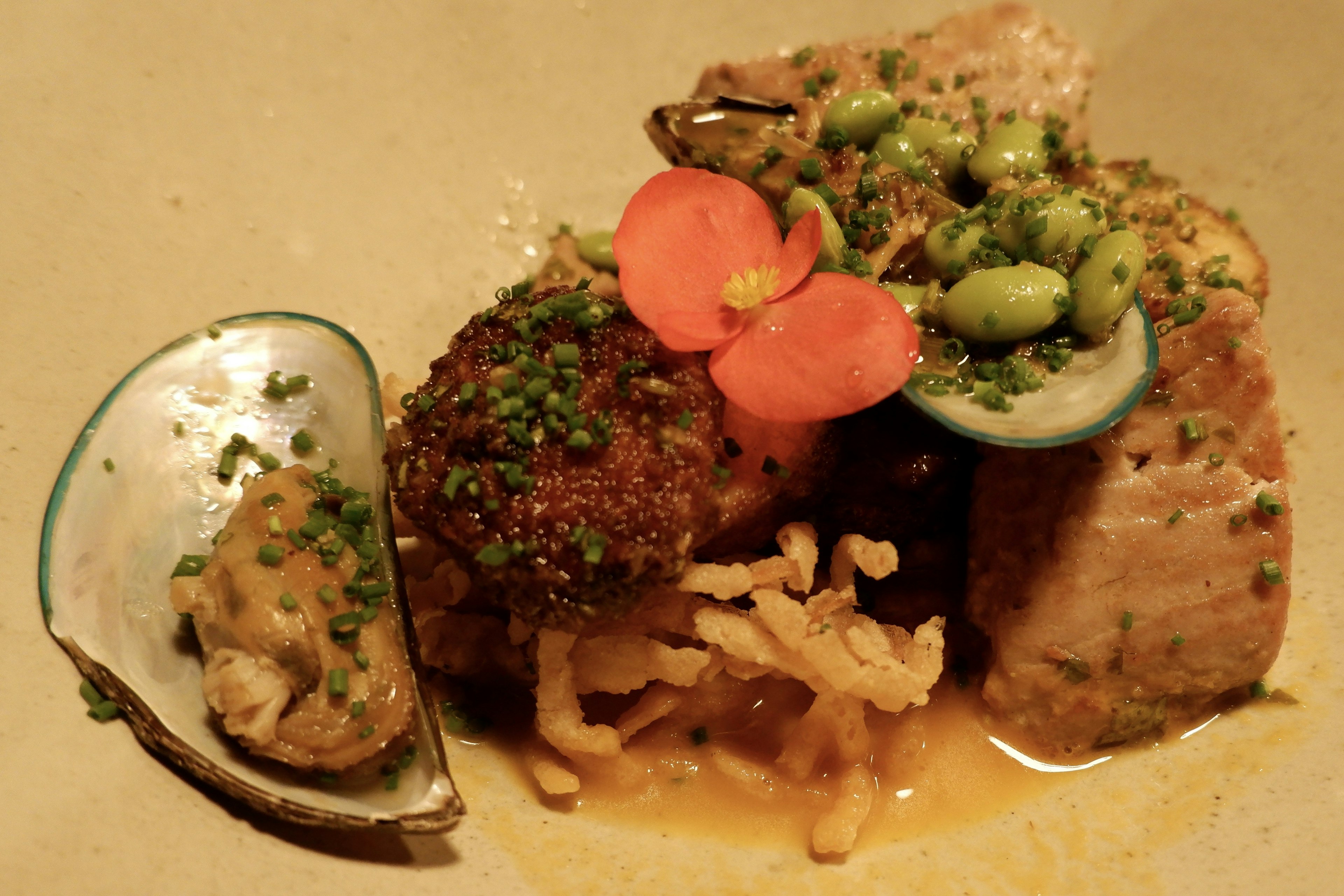 Closeup of a plate of food containing an open oyster next to seared piece of meat laying in yellow sauce.