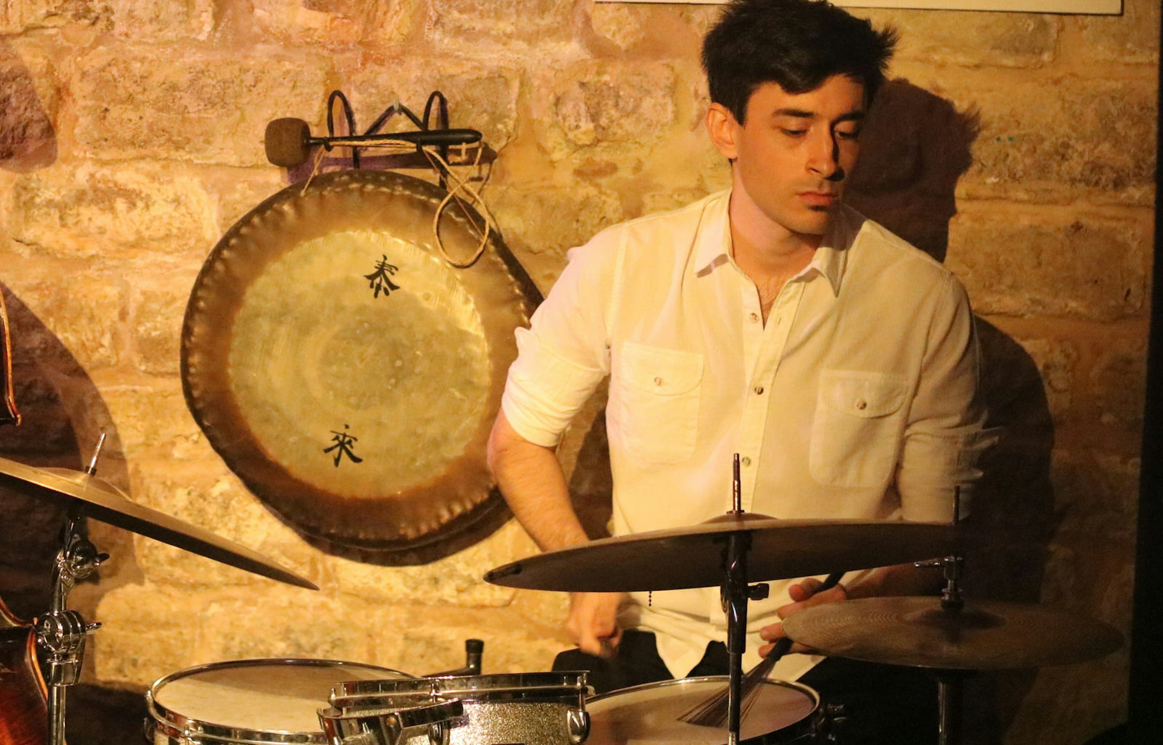 Backed by an old stone wall, which is adorned with an old Chinese gong, a drummer - sticks in hand - plays his drums © Catherine Le Nevez / Lonely Planet