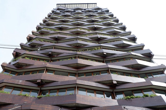 Low angle shot of the exterior of a brick hotel in El Poblado Medellin. There are large planters filled with shrubs peeking over the edge.