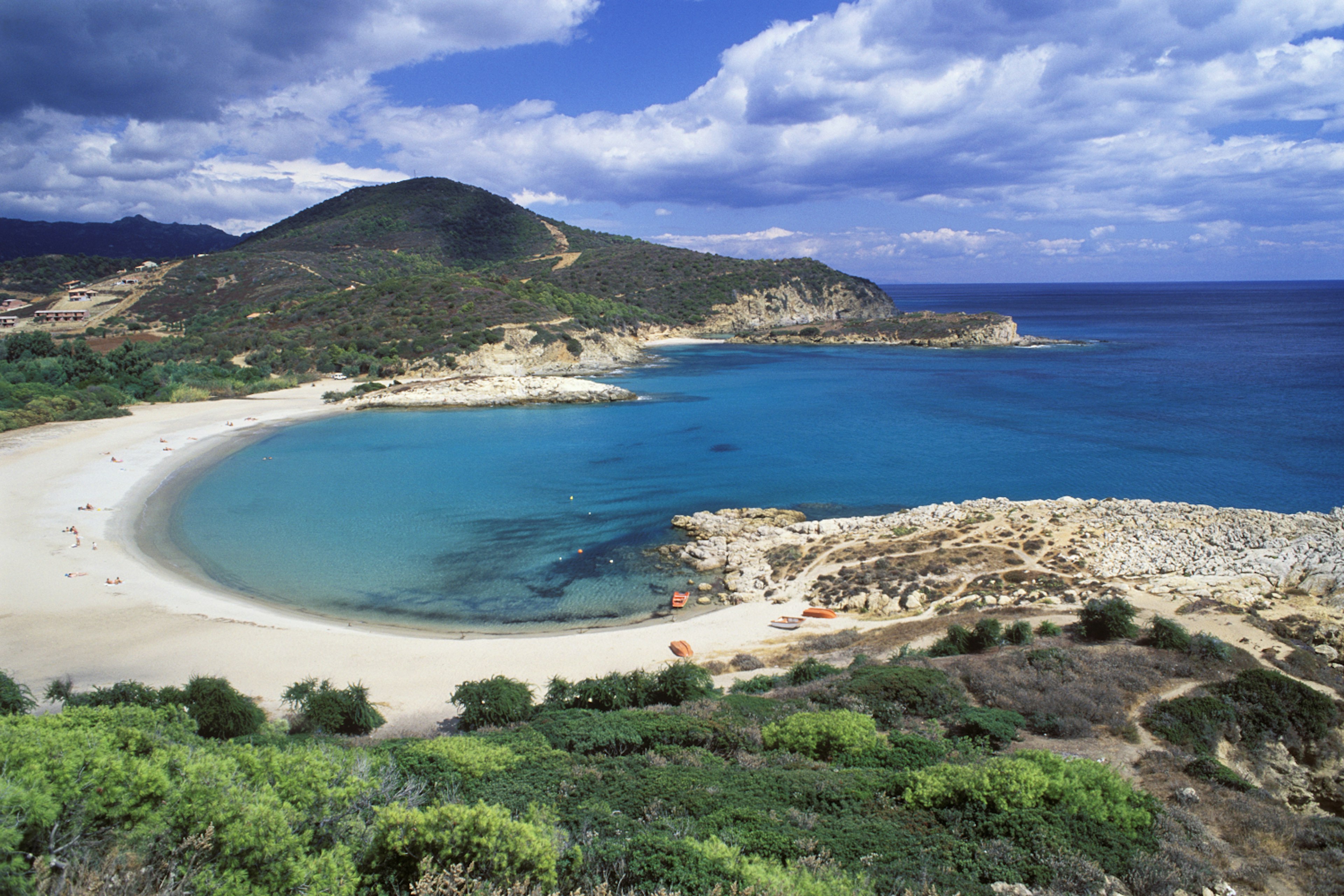 View of the horseshoe-shaped Spiaggia Su Portu, Sardinia, under partially cloudy skies.