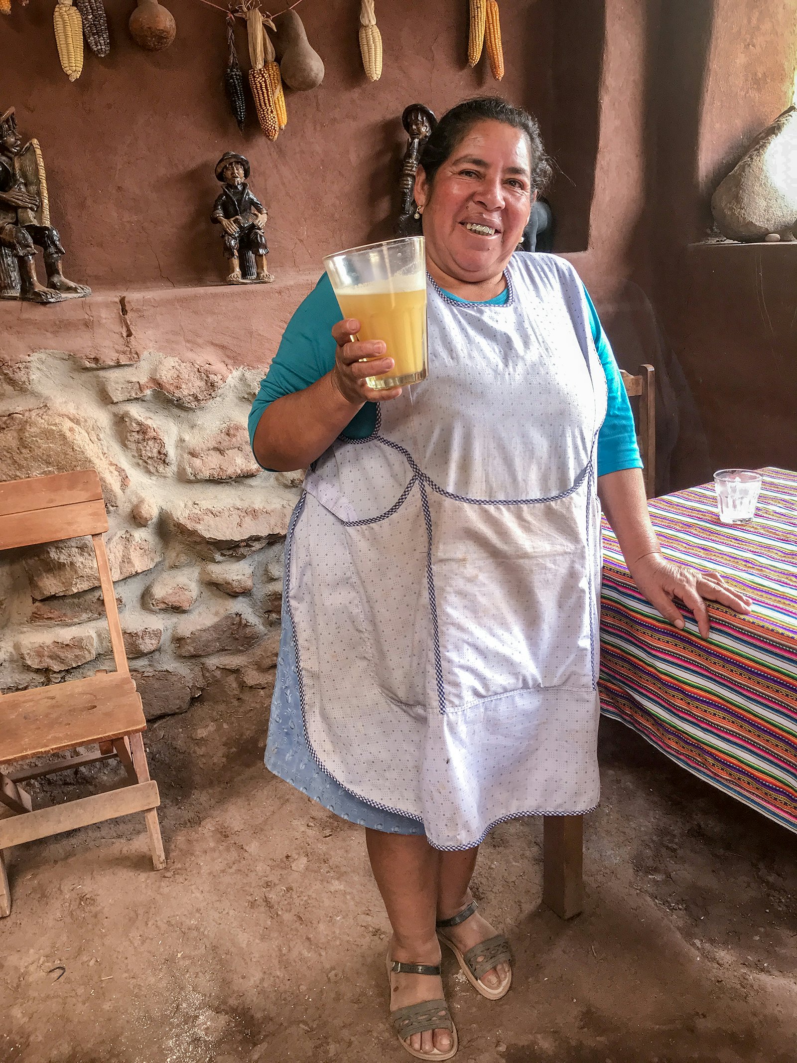 A woman in a white apron smiles at the camera, holding a large glass of beer