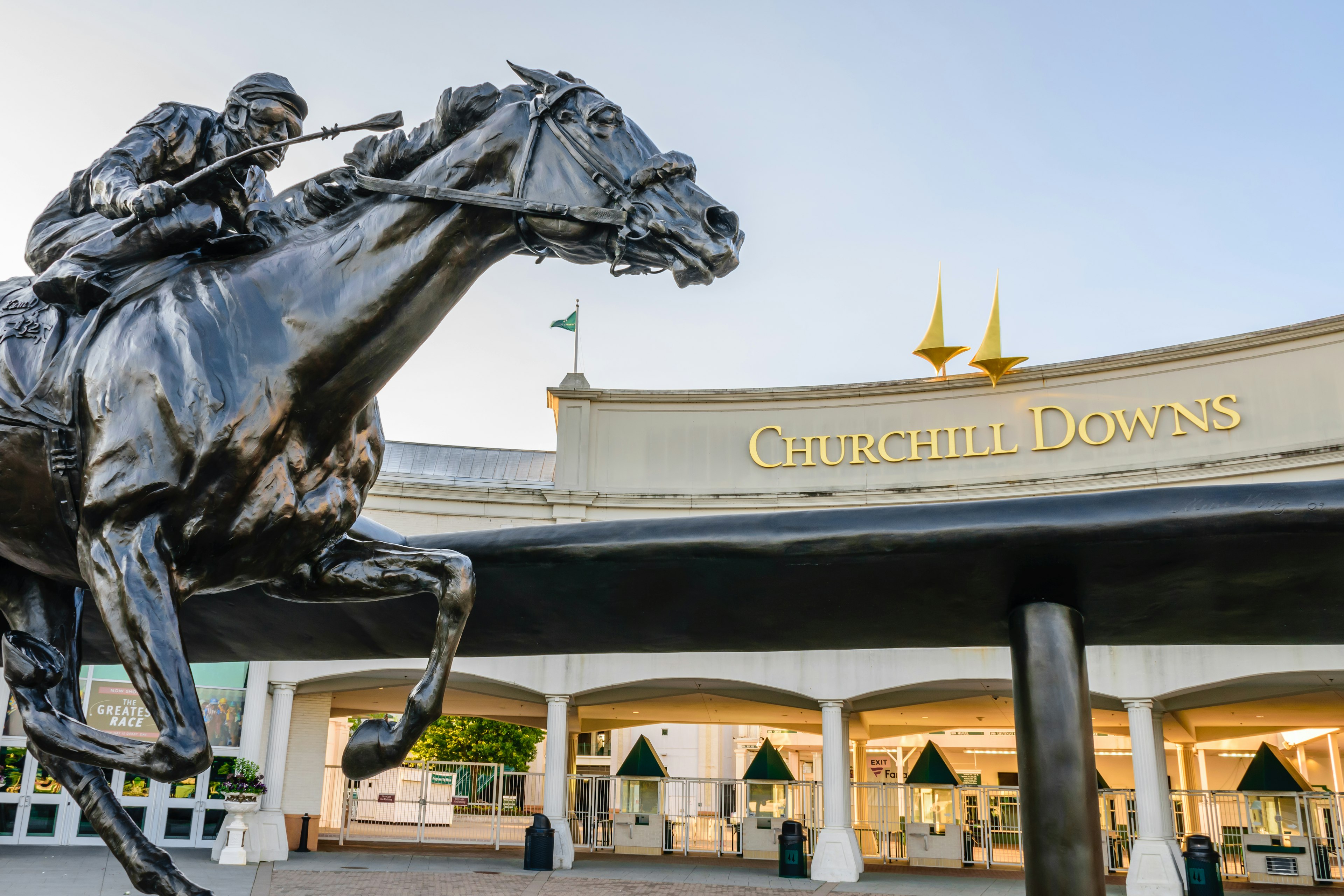 A statue of a jockey riding a horse sits outside the entrance to Churchill Downs.