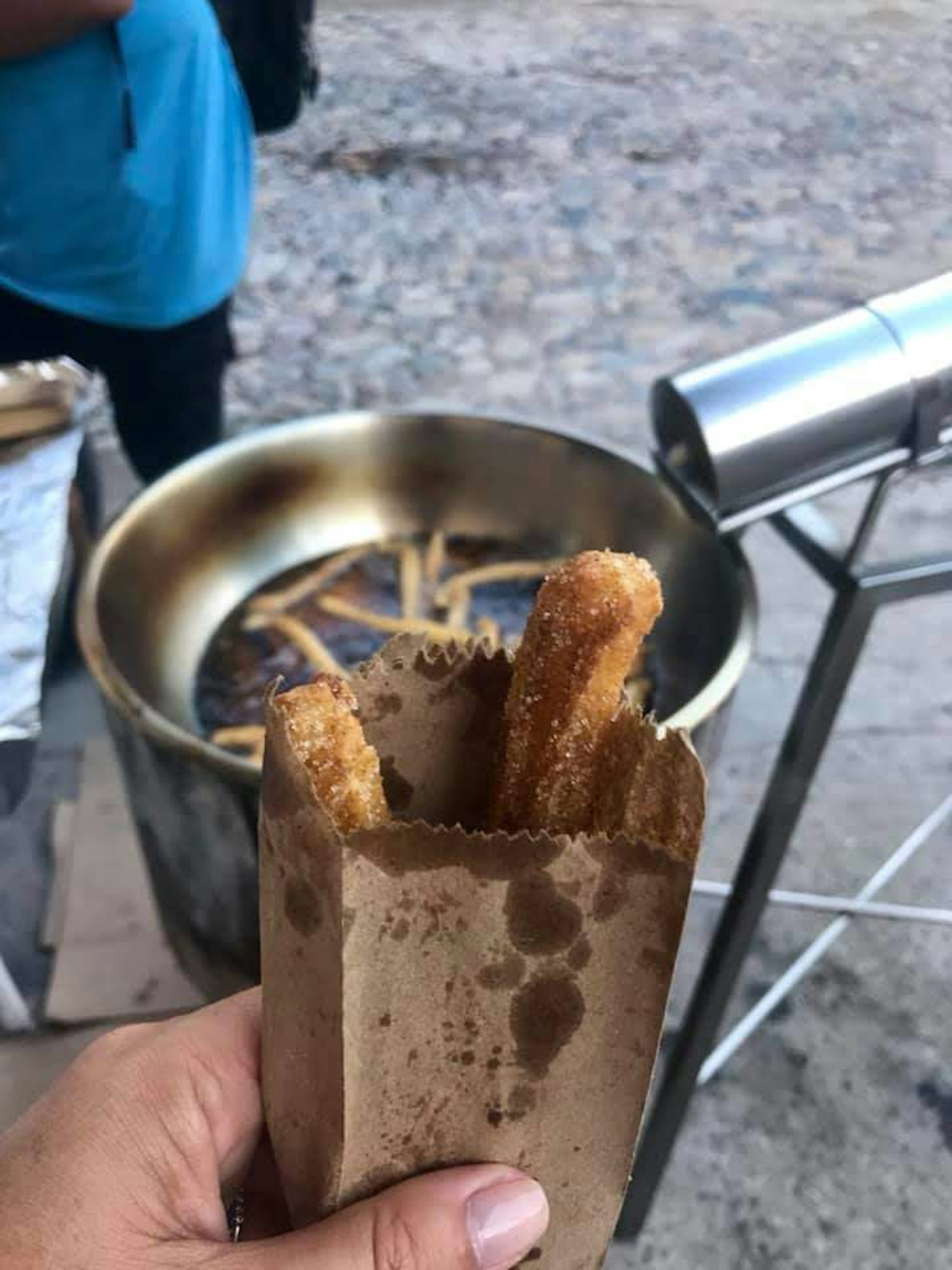 A hand holds an oiled-stained brown paper bag filled with two fresh churros, dusted with sugar, on a street in Puerto Vallarta