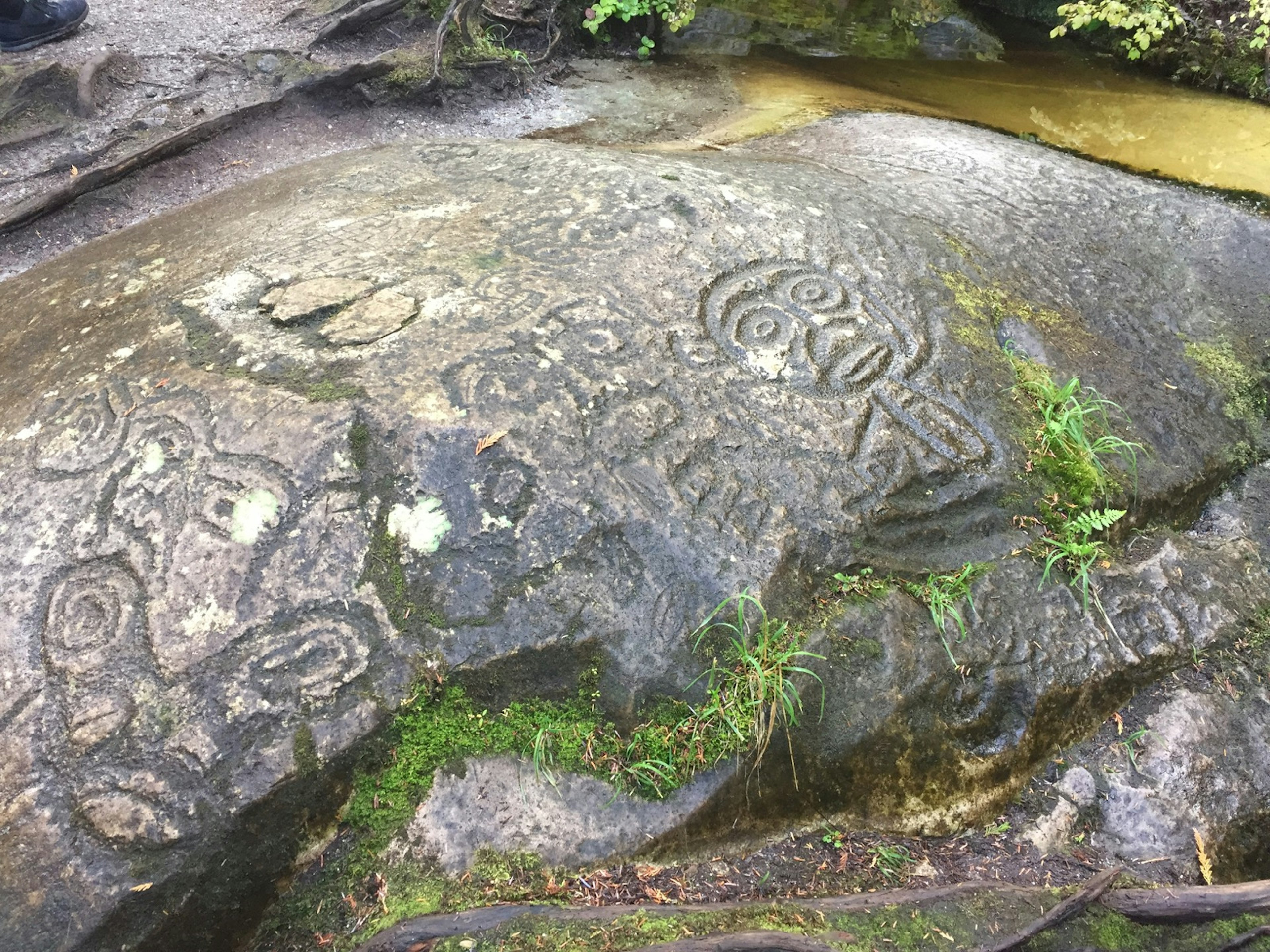 A broad, flat stone is covered in intricate stone carvings, including that of a man with short curly hair