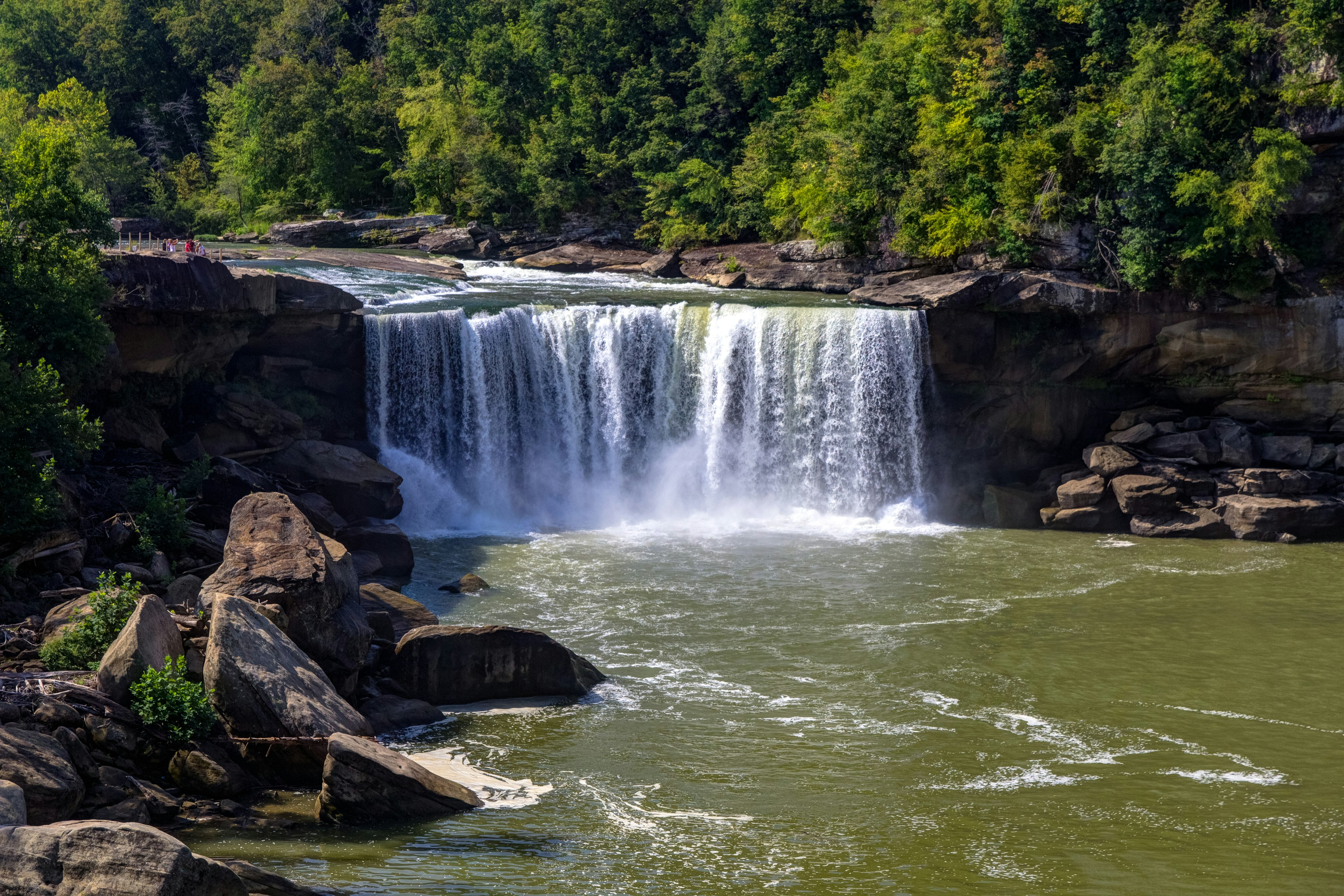 Waterfalls into green river water, with rocks on either side