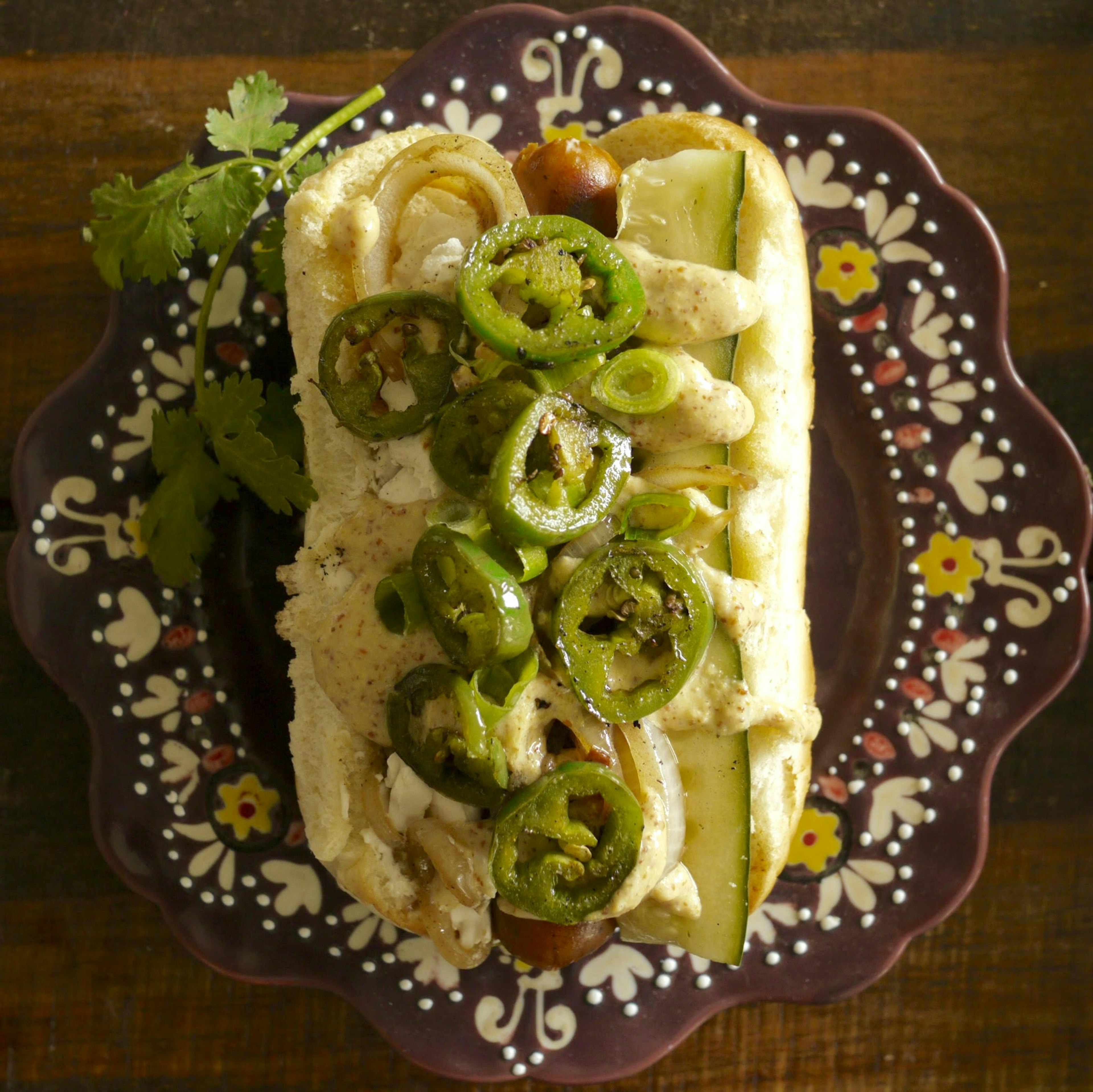 Closeup of a vegan hotdog piled high with onions, vegan cheese curds, jalapenos and mustard. There is a pickle stuffed on the side of the bun; vegan restaurants Seattle