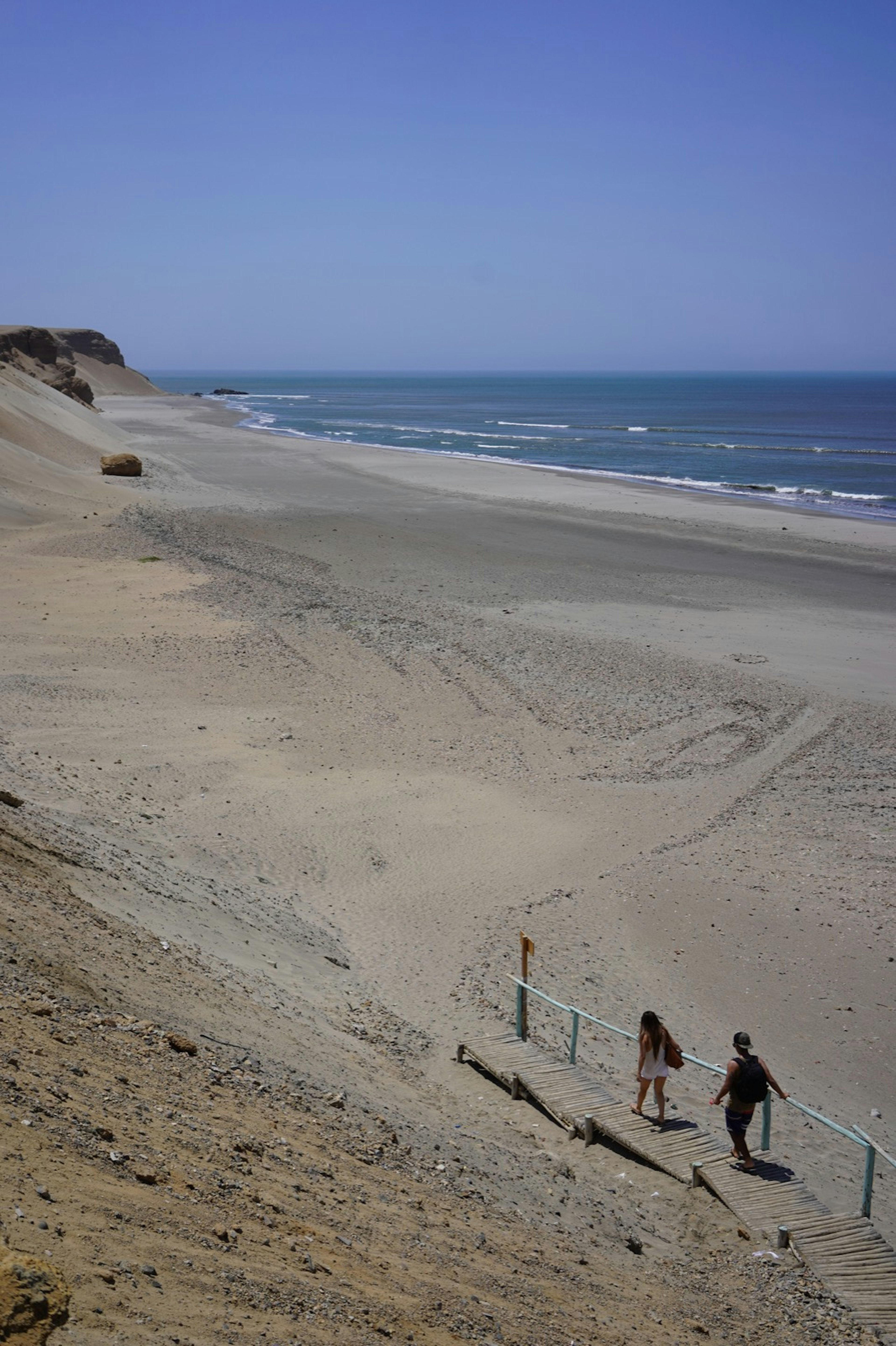 Two people scale steep stairs down to a deserted white sand beach