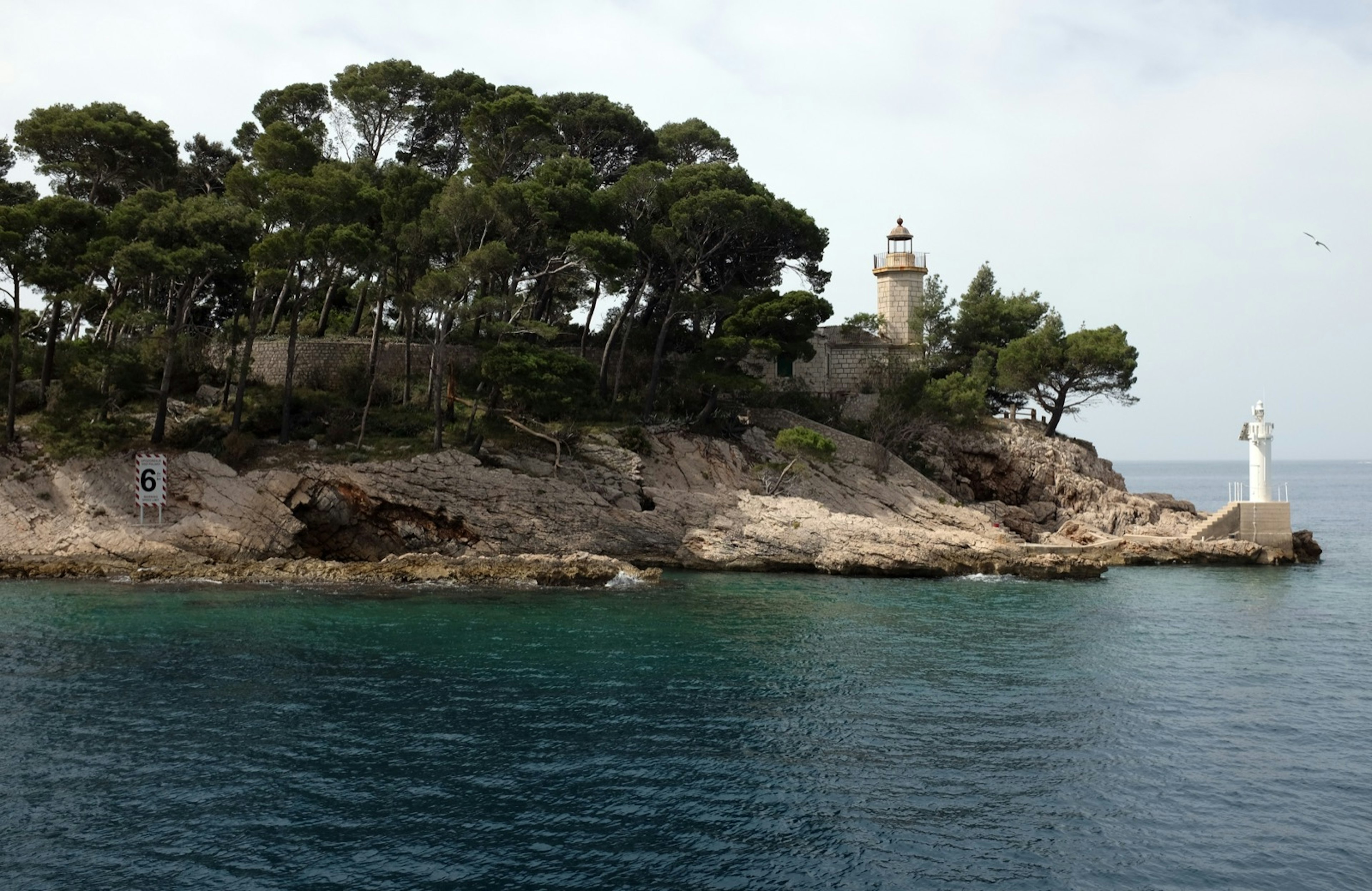 Trees cover a rocky coast; there is a white structure on a rock jutting into the sea; haunted places world