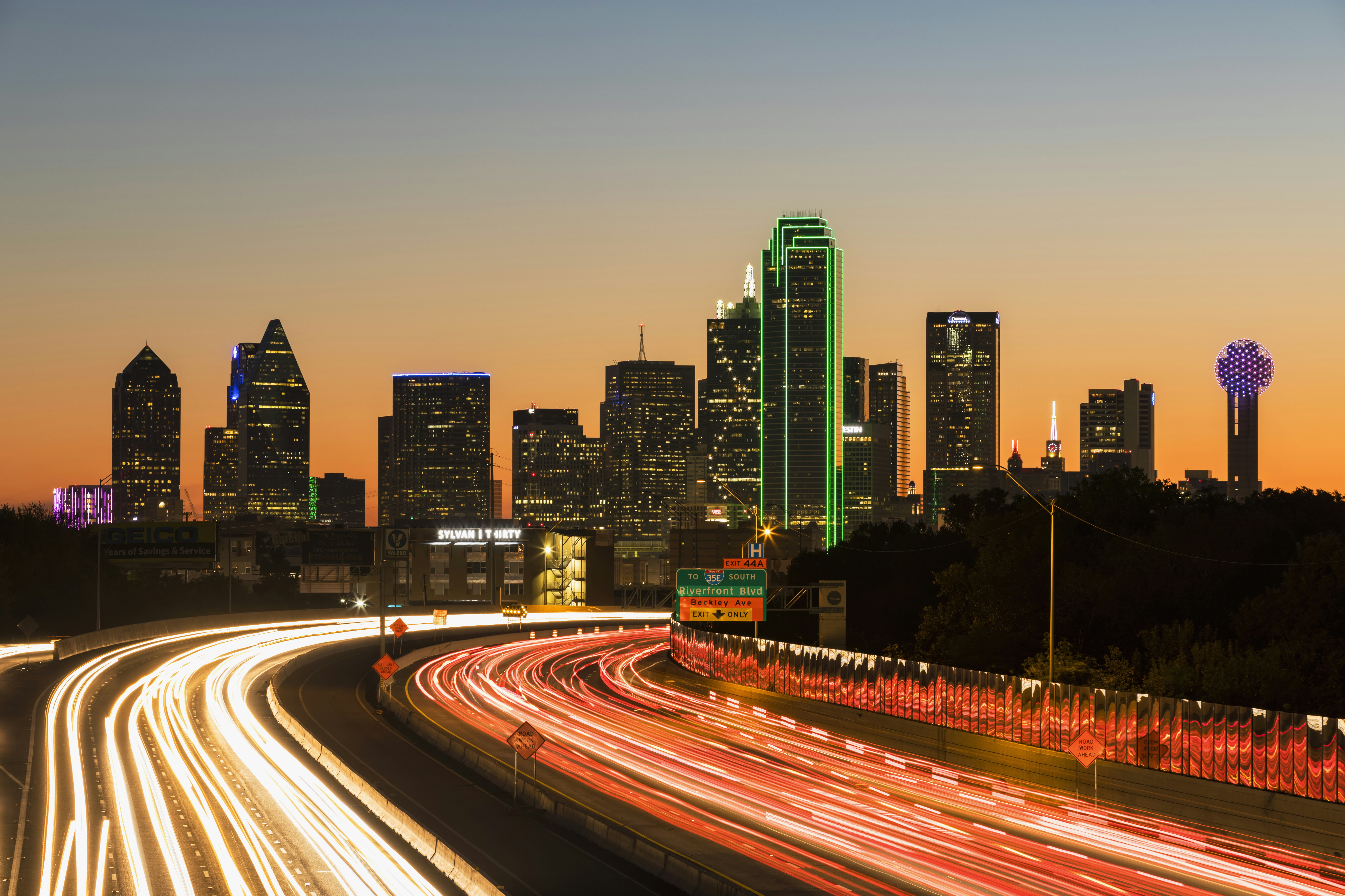 Buildings making up the downtown skyline shine bright in the night sky. Below is a blur of headlights on the highway; Thanksgiving NFL city