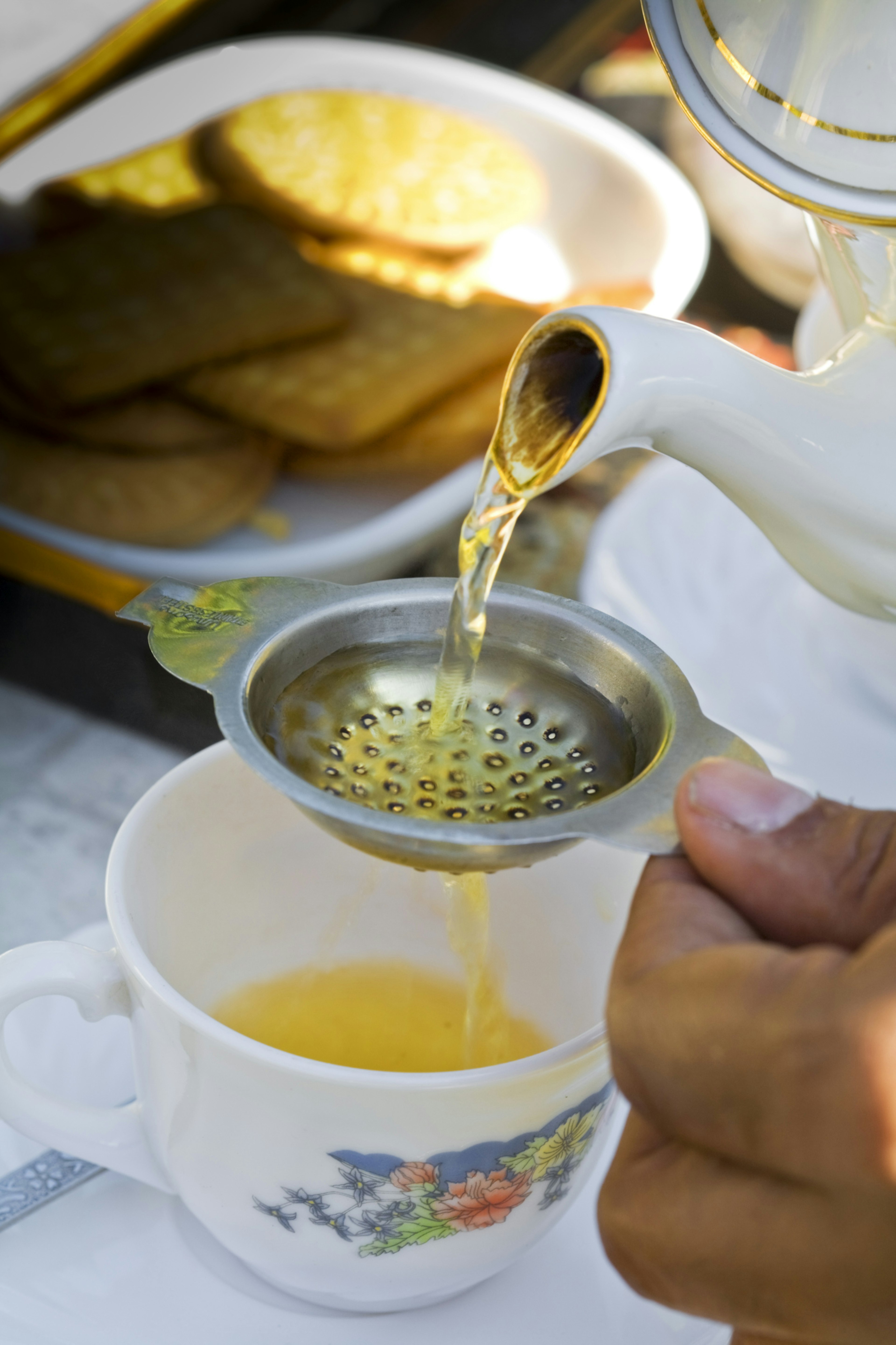 Tea being poured from a teapot into a filter and onwards into a white cup