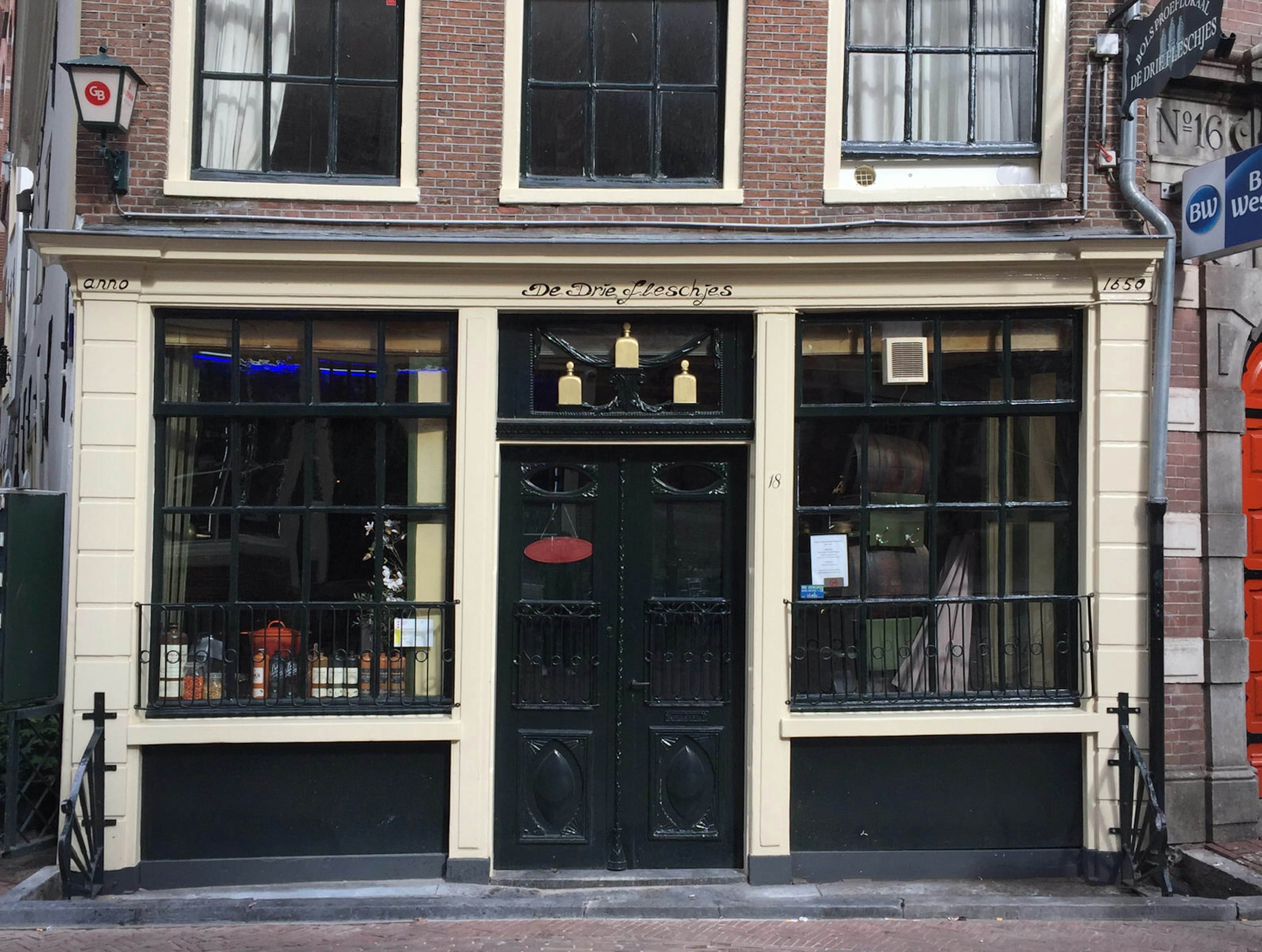 An old brick building with wooden-framed windows (painted dark green) on a cobbled street in Amsterdam; it's one of the best places to sip jenenver in Amsterdam