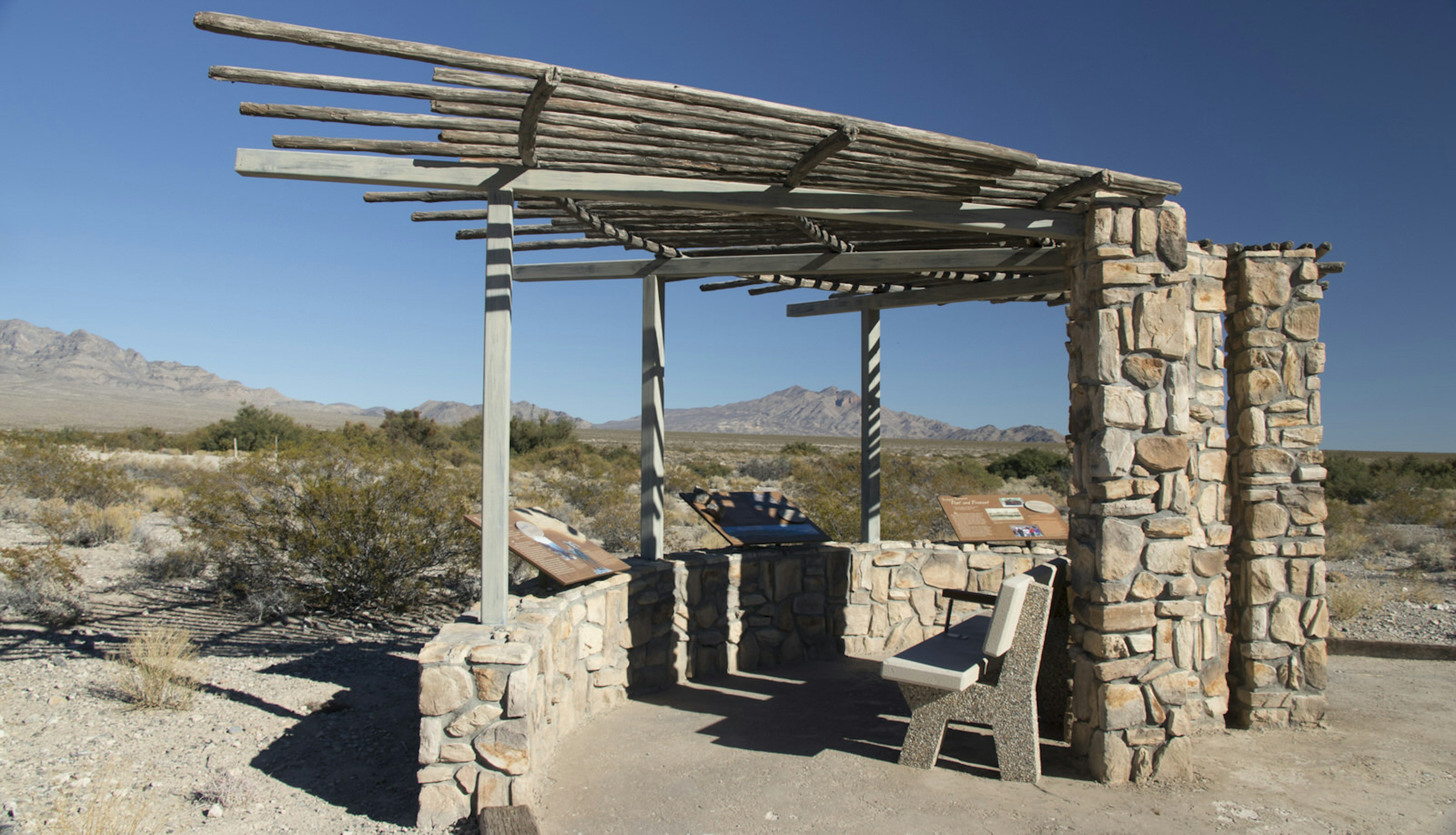 An expansive vista of scrubland and desert stretches behind a very ramshackle information gazebo made of stone and reclaimed wood © Greg Thilmont / Lonely Planet