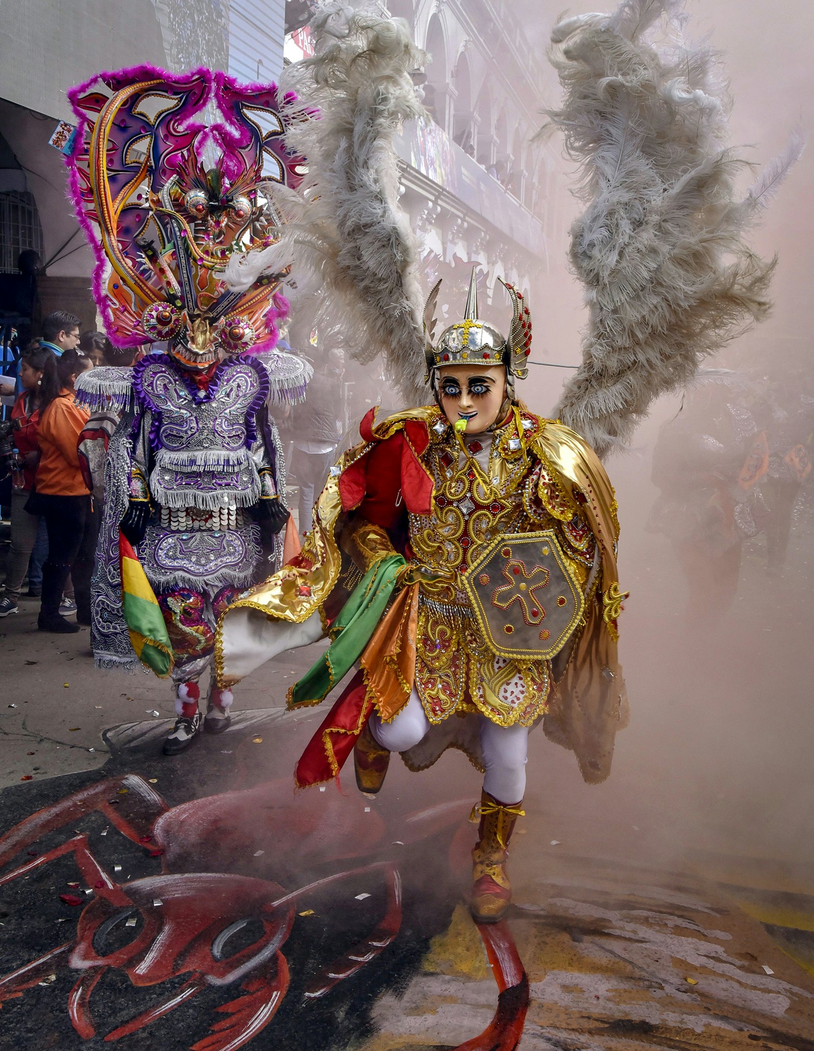 A man dressed in an elaborately ornate angel costume runs through smoke during during Diablada during Carnival in Bolivia