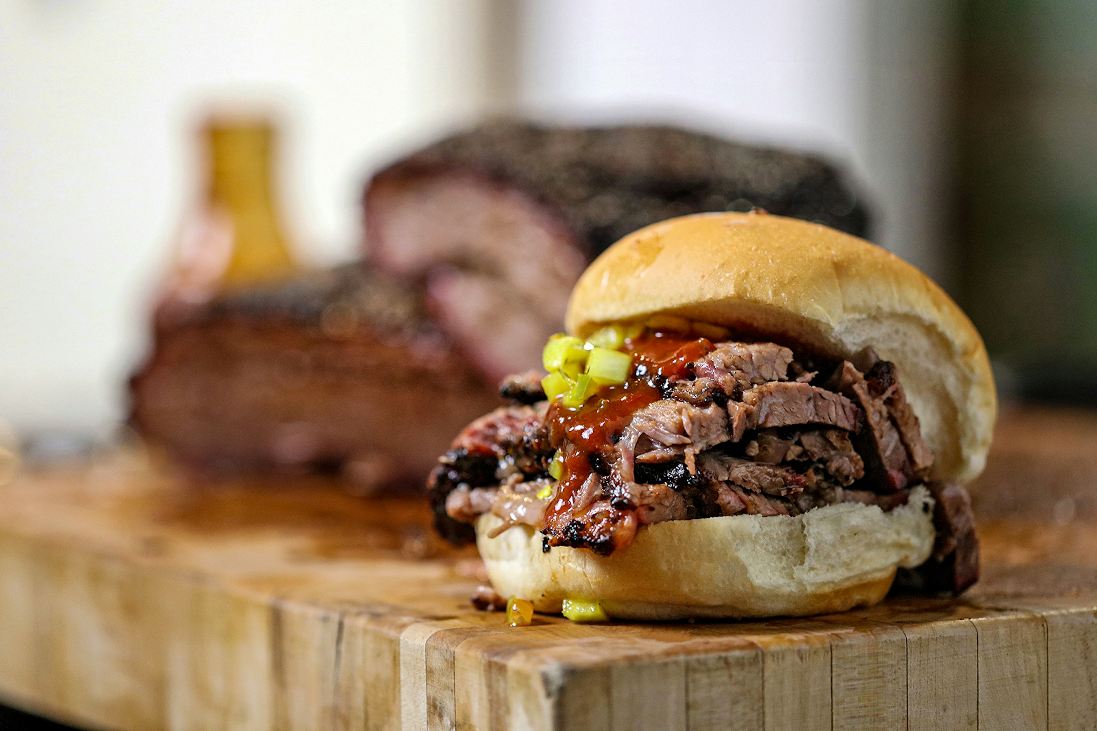 A close-up of a barbecue sandwich filled with beef, sauce and pickles sitting on a butcher block counter. Buffalo, New York.