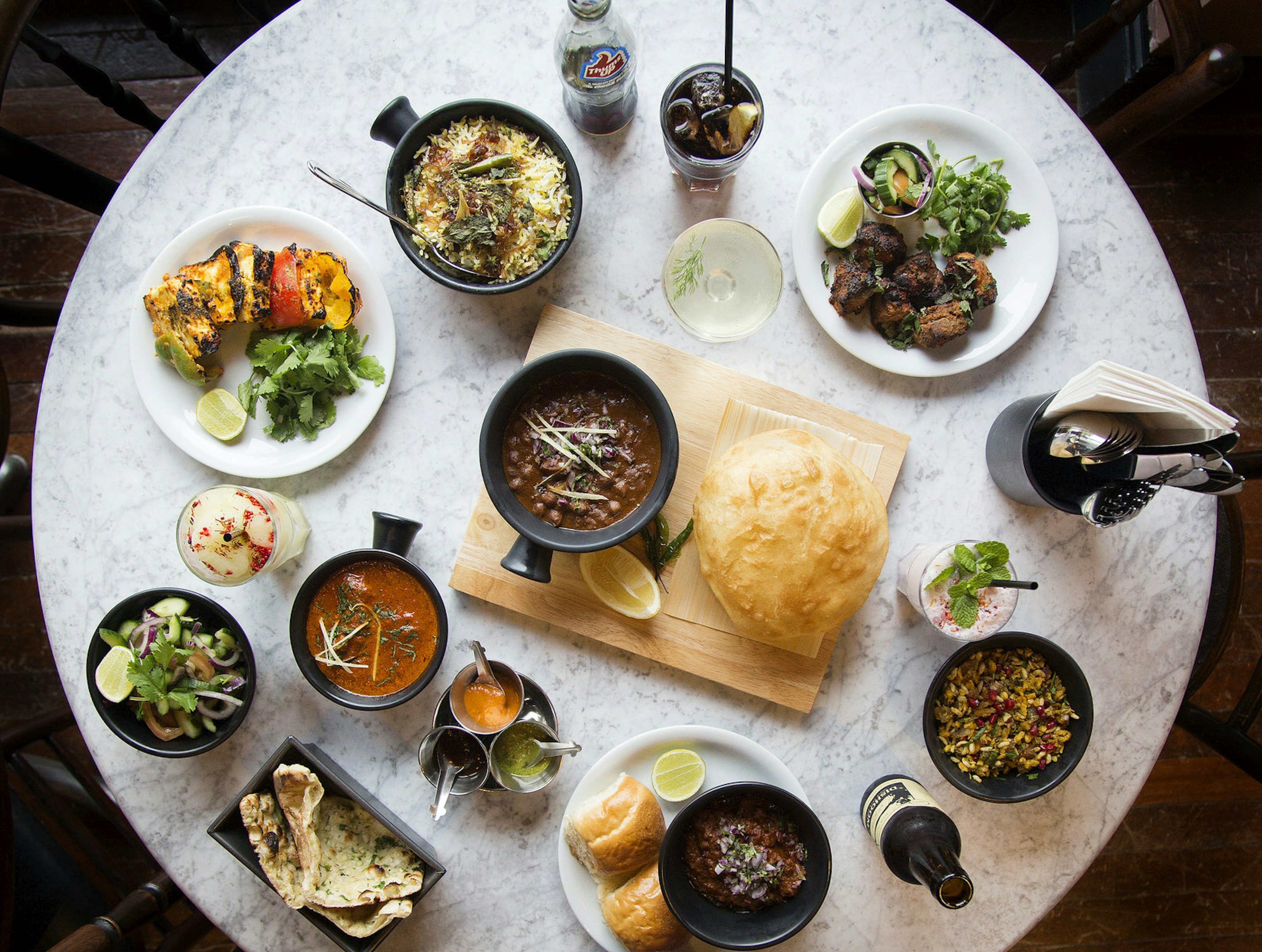 An aerial shot of a round, marble-topped table laden with several dishes and drink at Dishoom, Edinburgh.