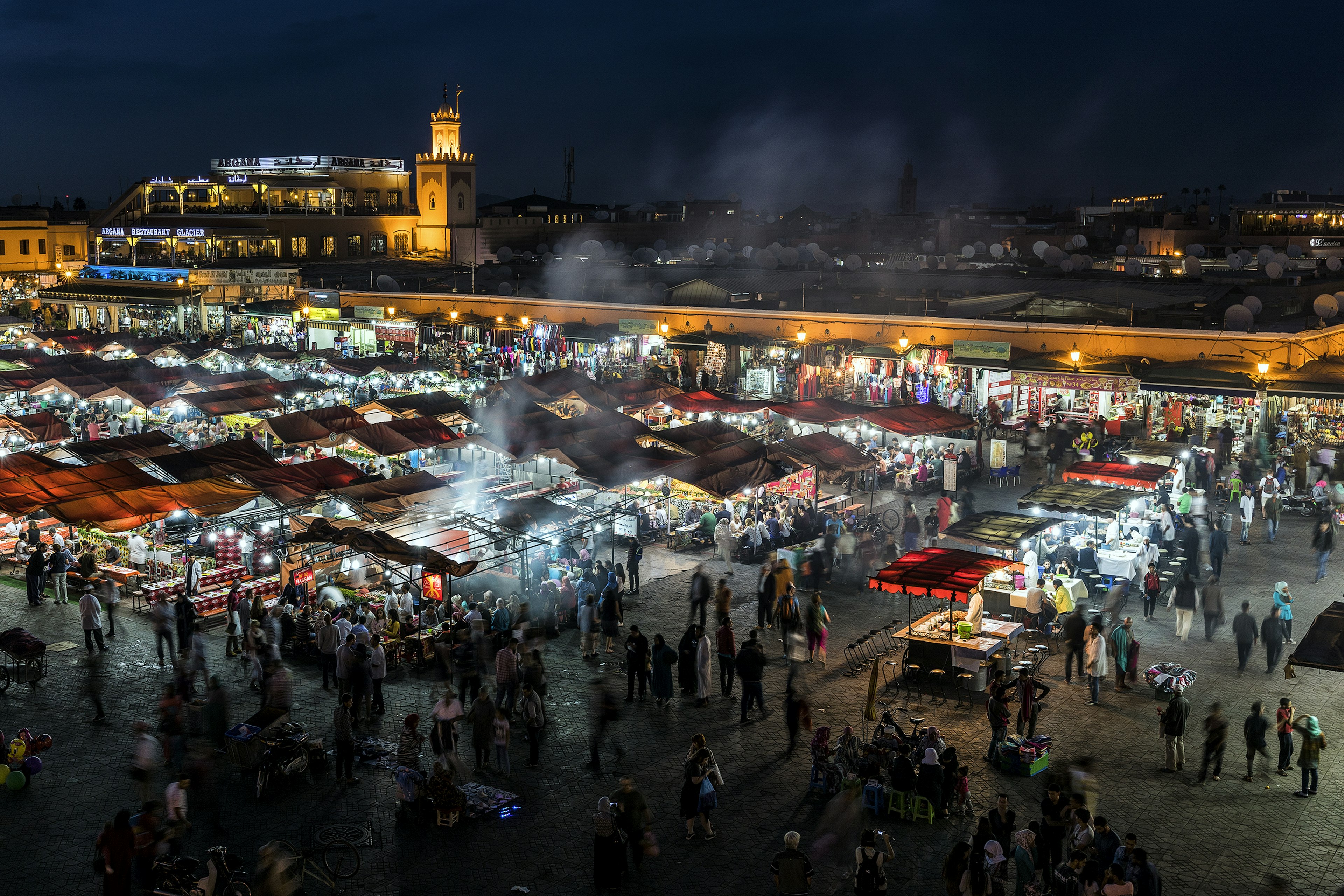 A market square at night with people milling around food stalls cooking fresh dishes