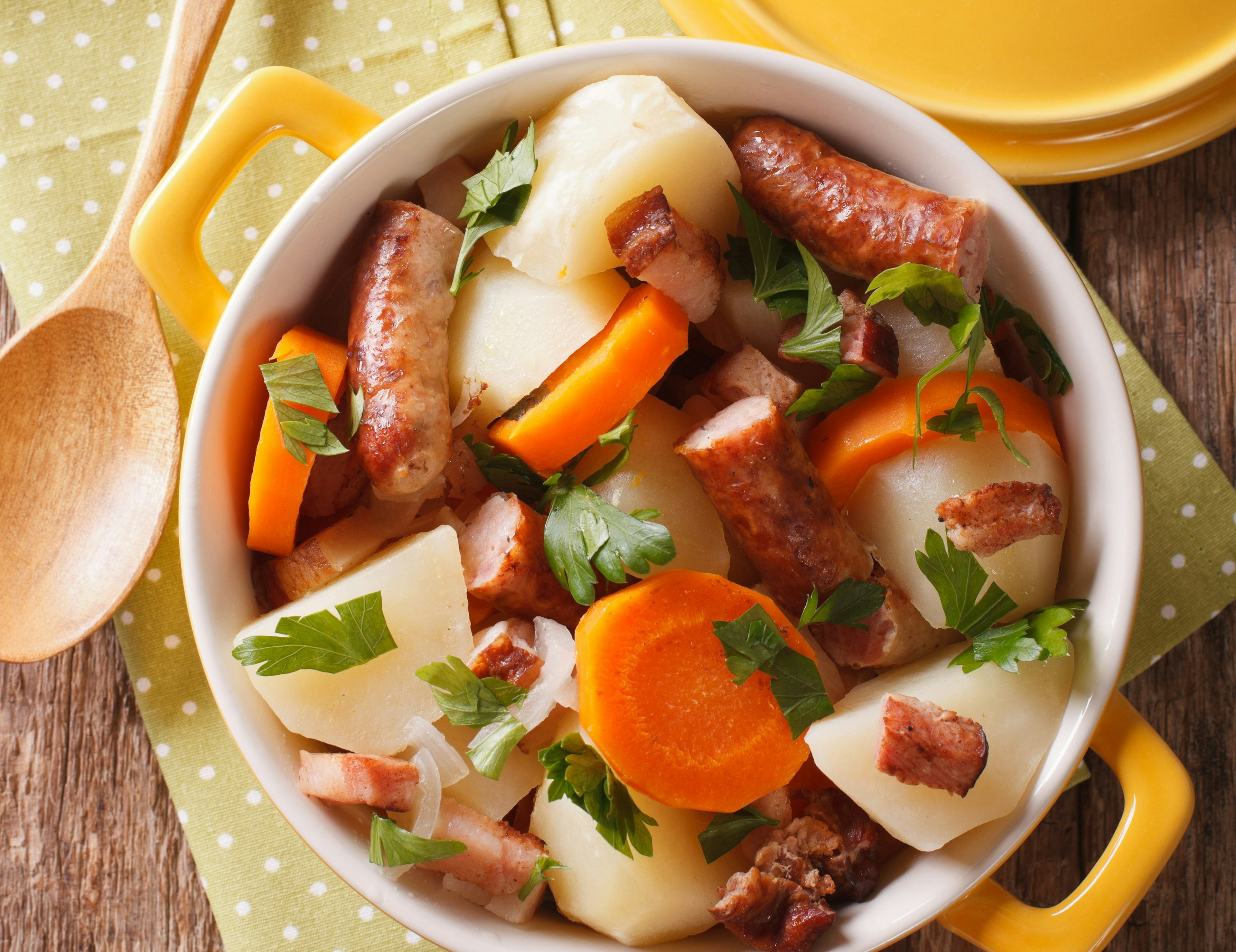 A Dublin Coddle, as seen from above. The stew is served in a round bowl on a tabletop and contains sausage, potato and carrot and is garnished with parsley.