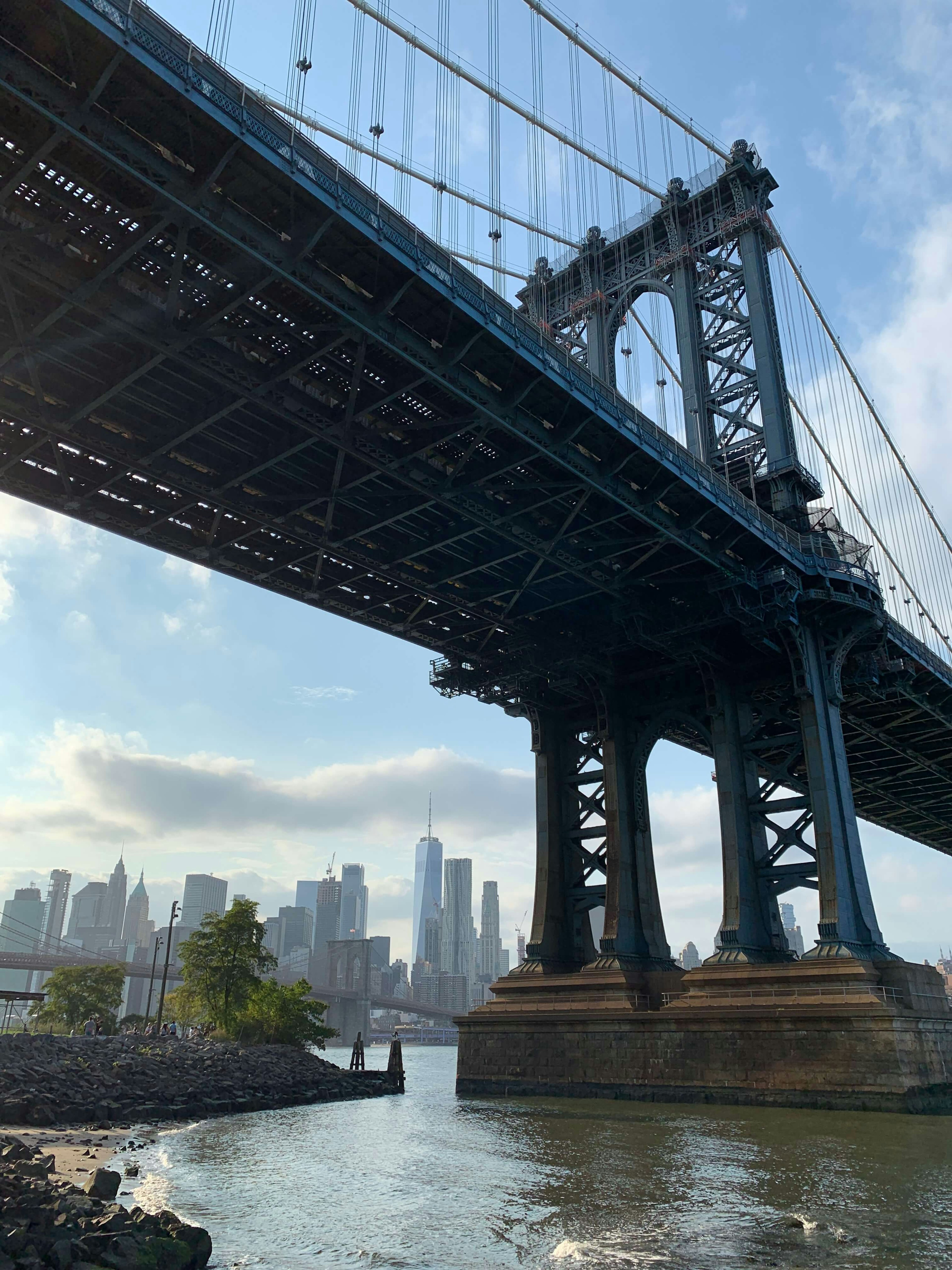 A view of the Brooklyn Bridge from underneath, with Manhattan skyscrapers in the background