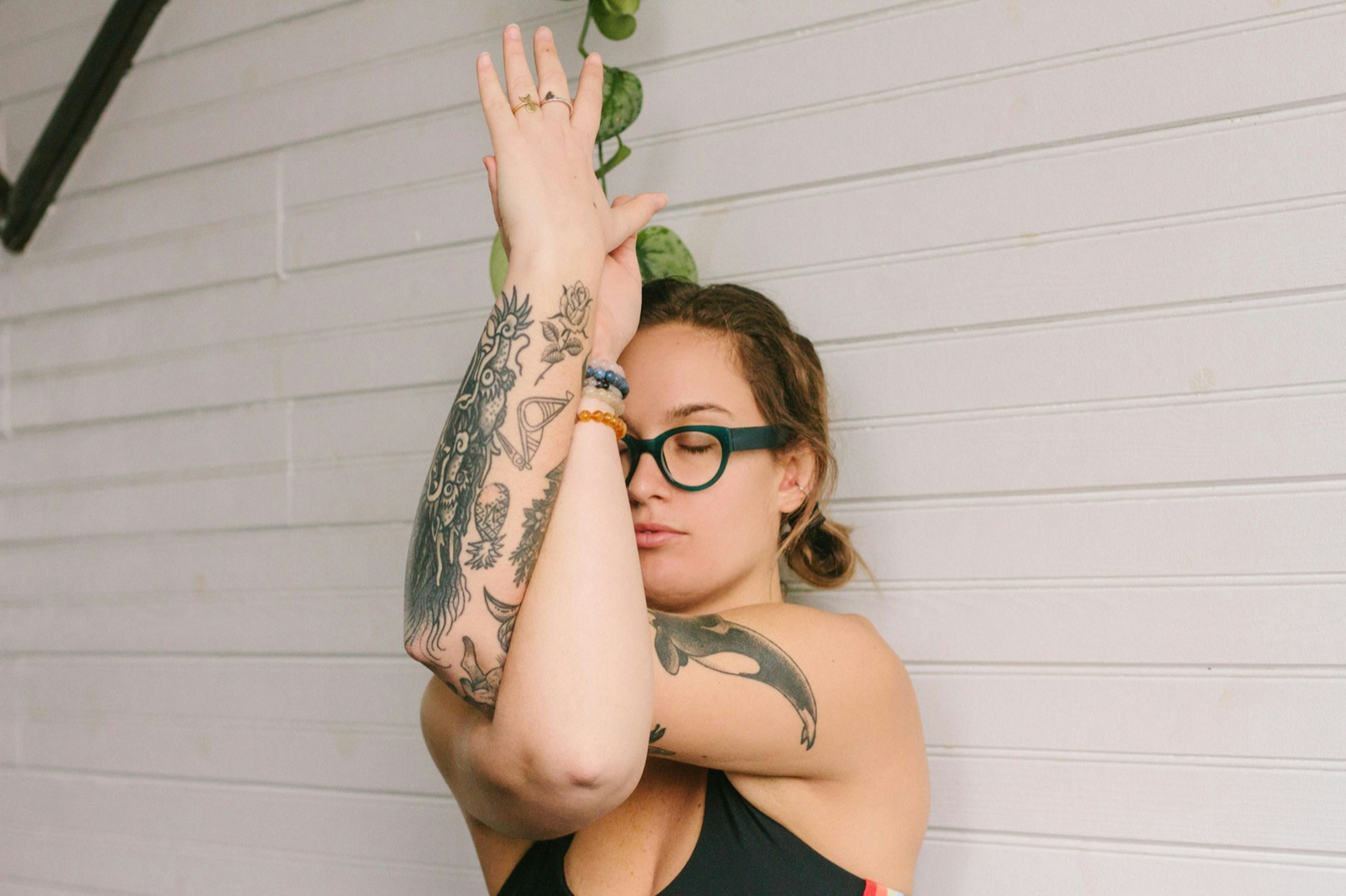 Woman performs the eagle arms yoga pose on a backdrop of a white wall