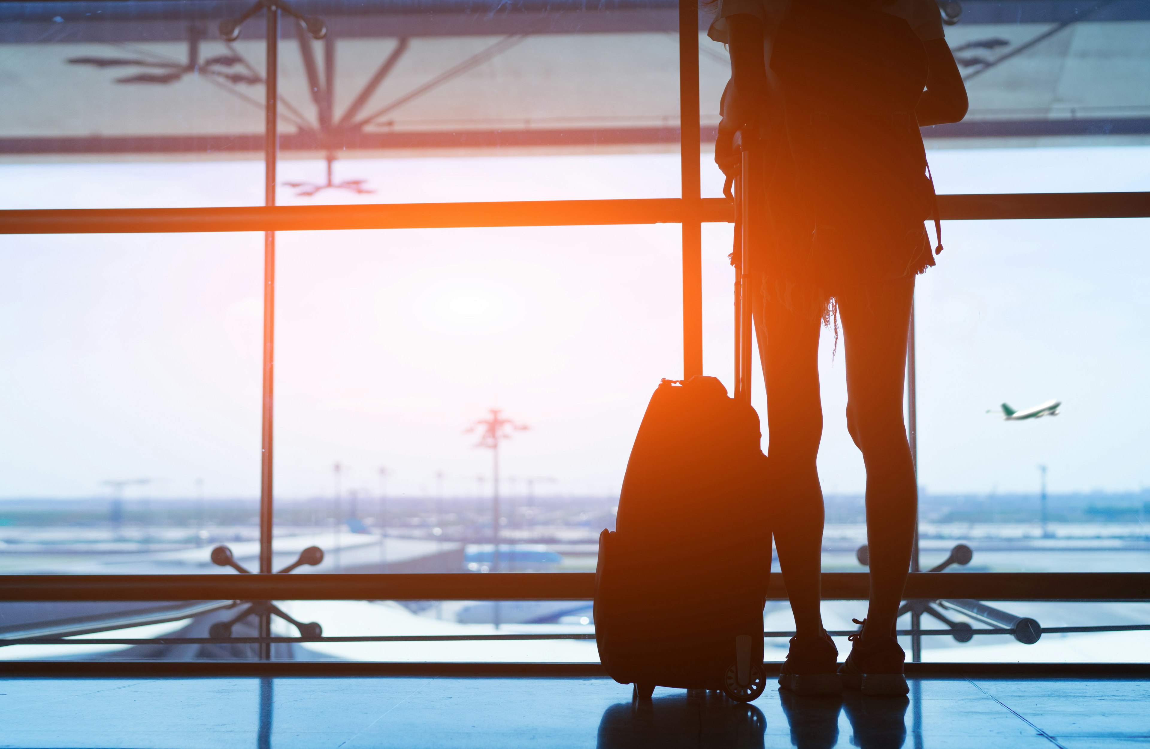 Silhouetted woman standing with her luggage at an airport terminal during sunset.