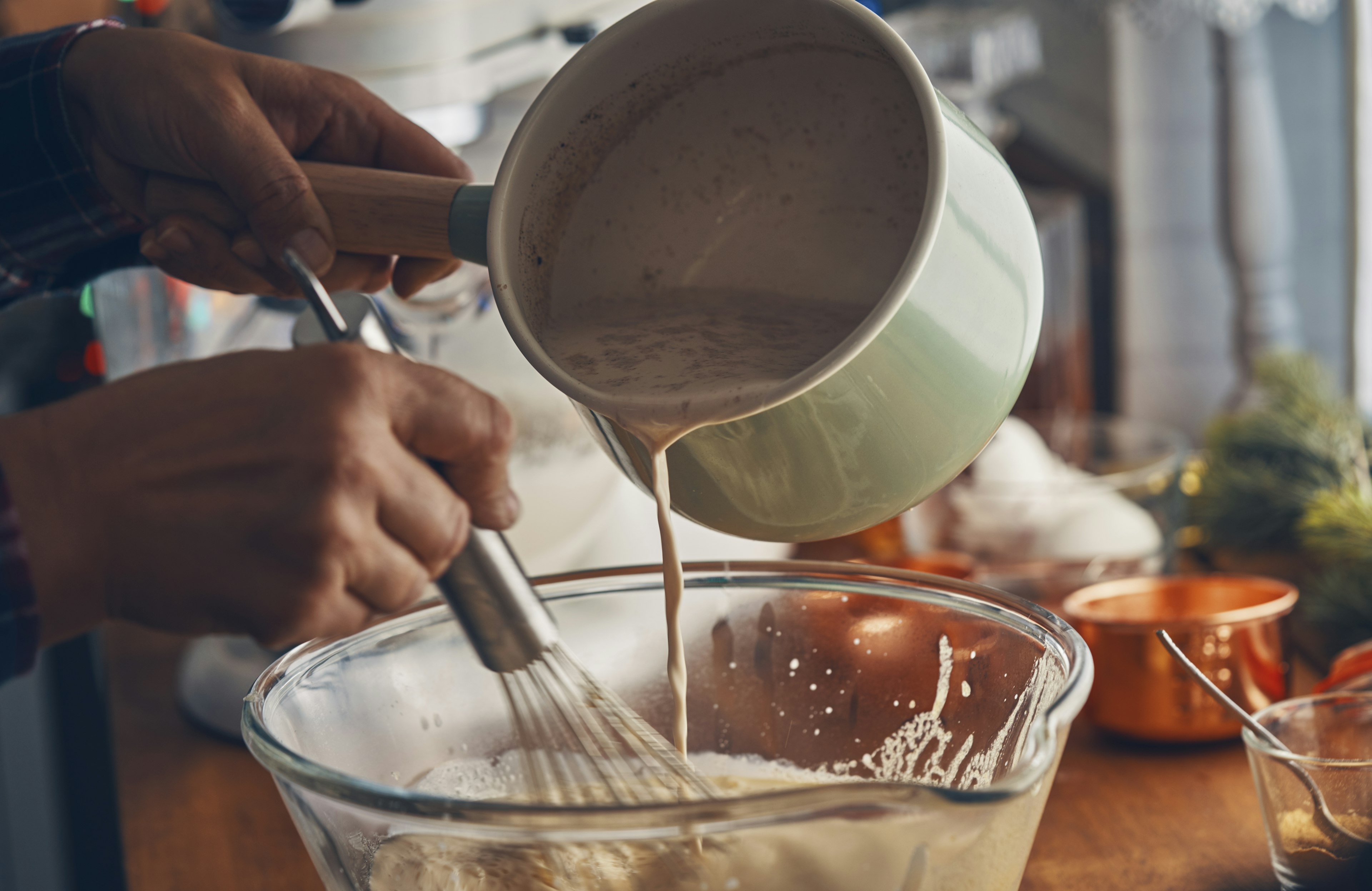 A person pours a creamy mixture into a glass bowl while whisking