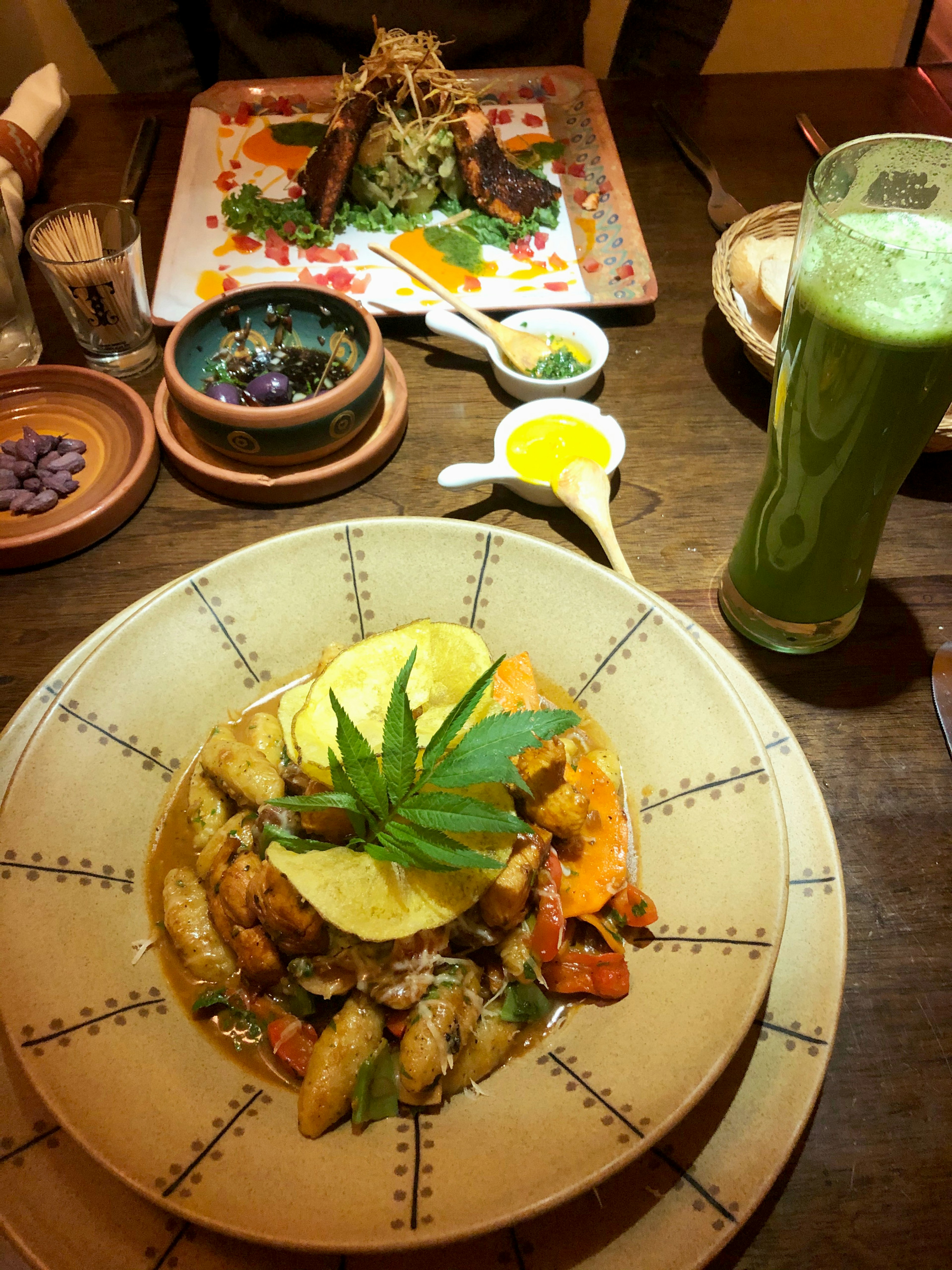 A meal of grilled trout and knochi with a green smoothie and a side dish of olives