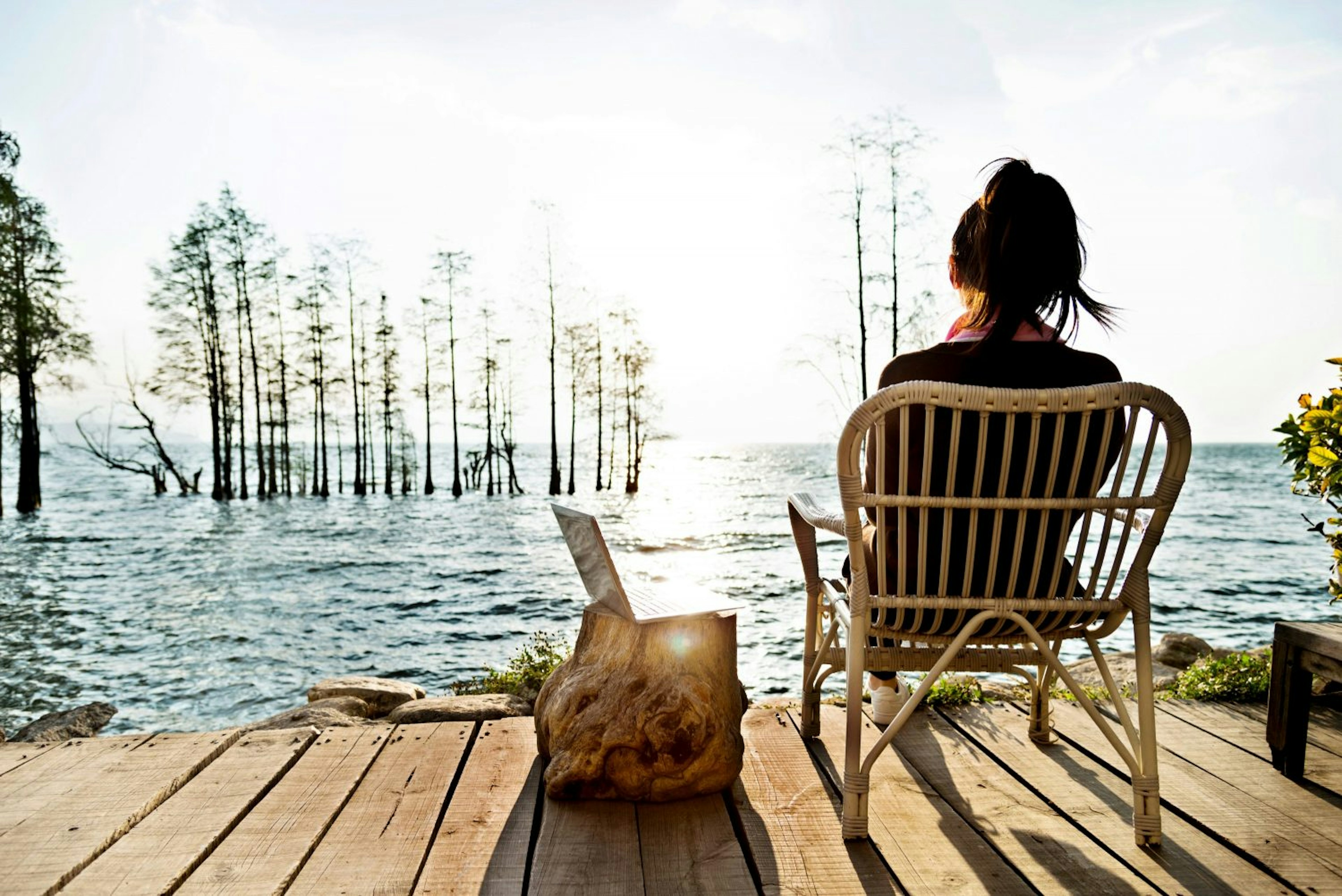 A woman working on her laptop while sitting by the lake.