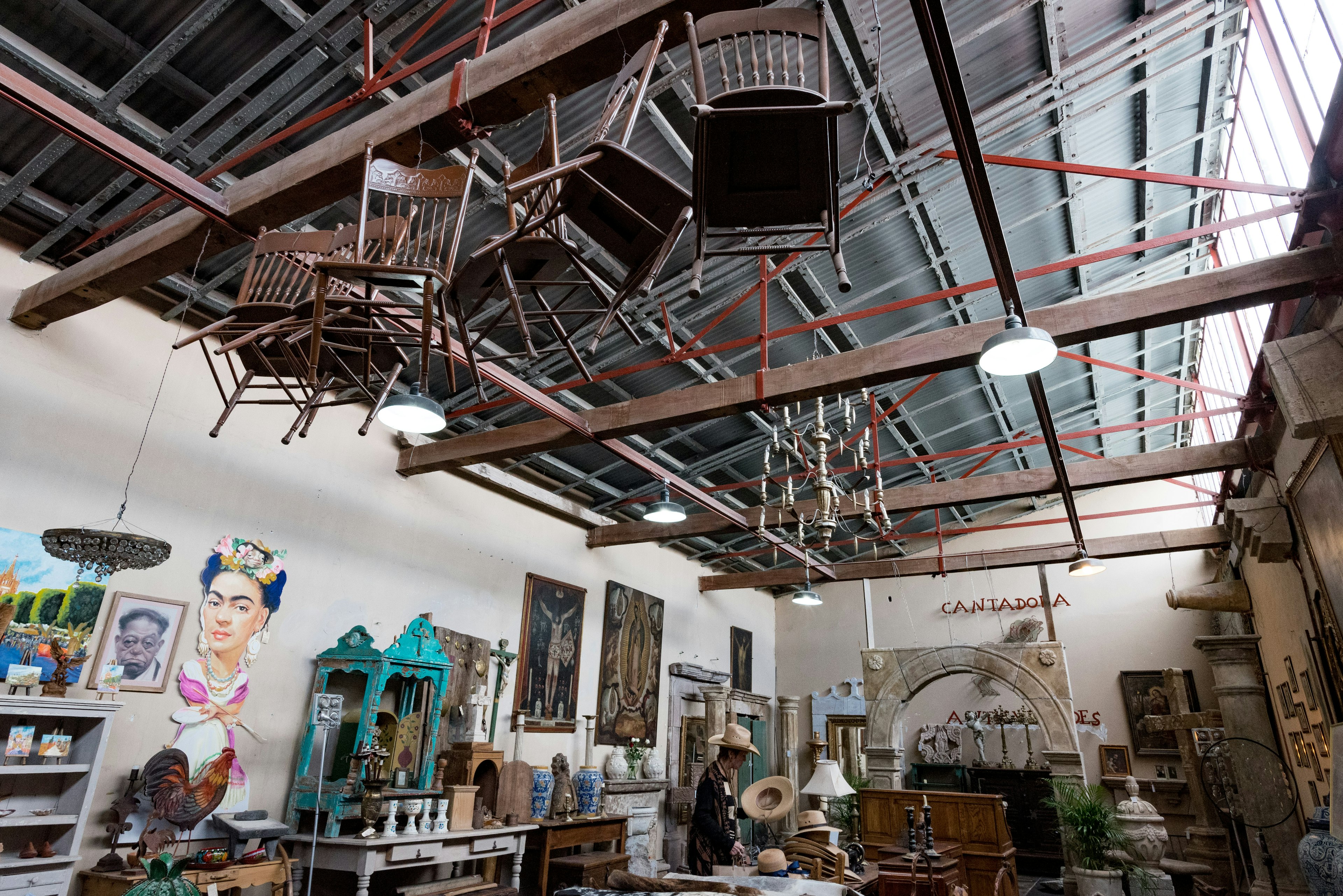 Chairs dangle from the wooden ceiling beams of a design complex, Fábrica La Aurora, where at ground level ornaments, homewares and antiques are on display