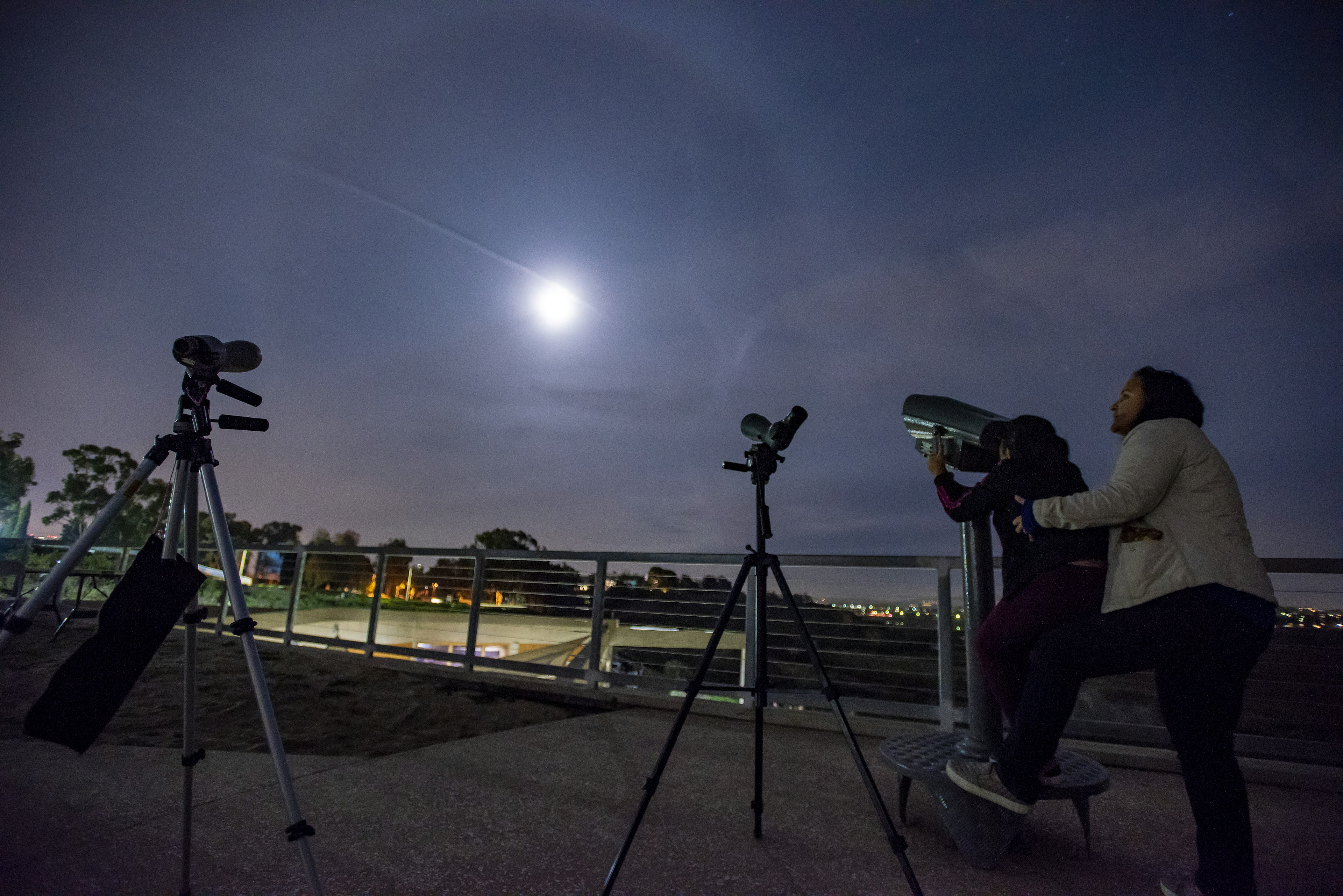 A woman helps a child look into a telescope on a starry night