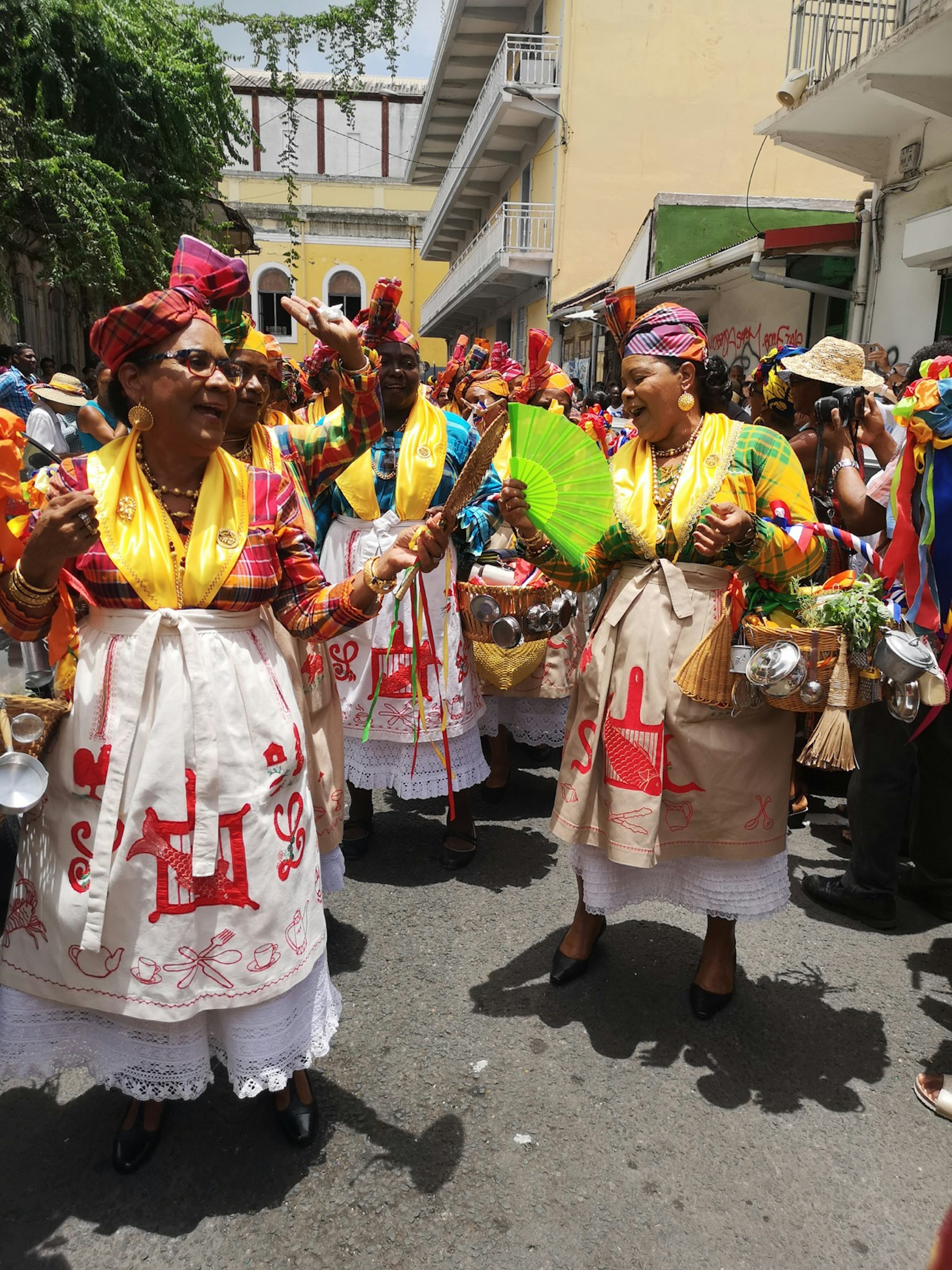 A group of women wearing traditional checkered tops and headwraps with white or brown aprons hold baskets filled with home-made treats during Fête des Cuisinières in Guadeloupe © Laura French/Lonely Planet