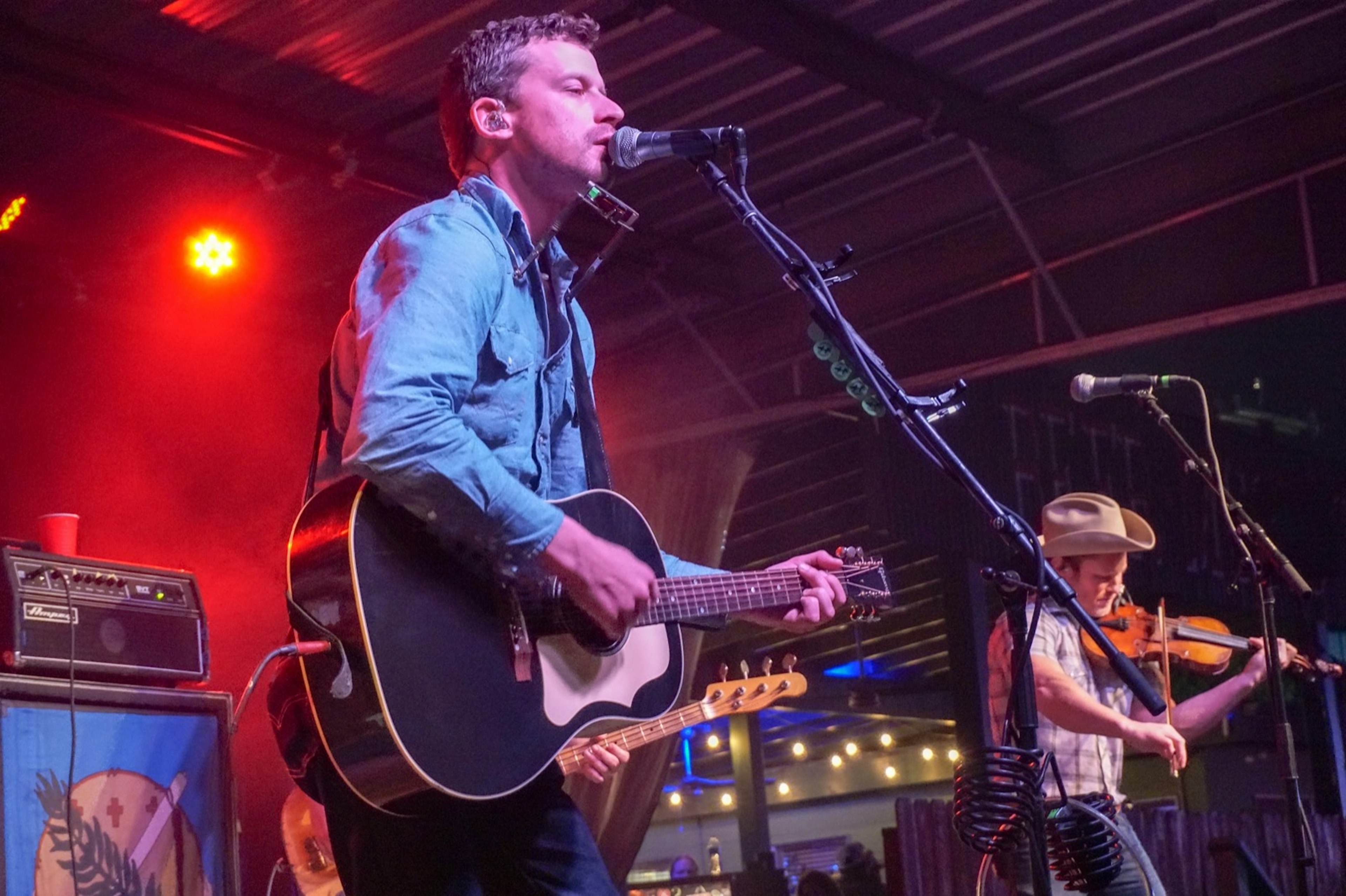 A country band with a guitar player and fiddle player play for a large crowd at a nighttime concert in the Hill Country