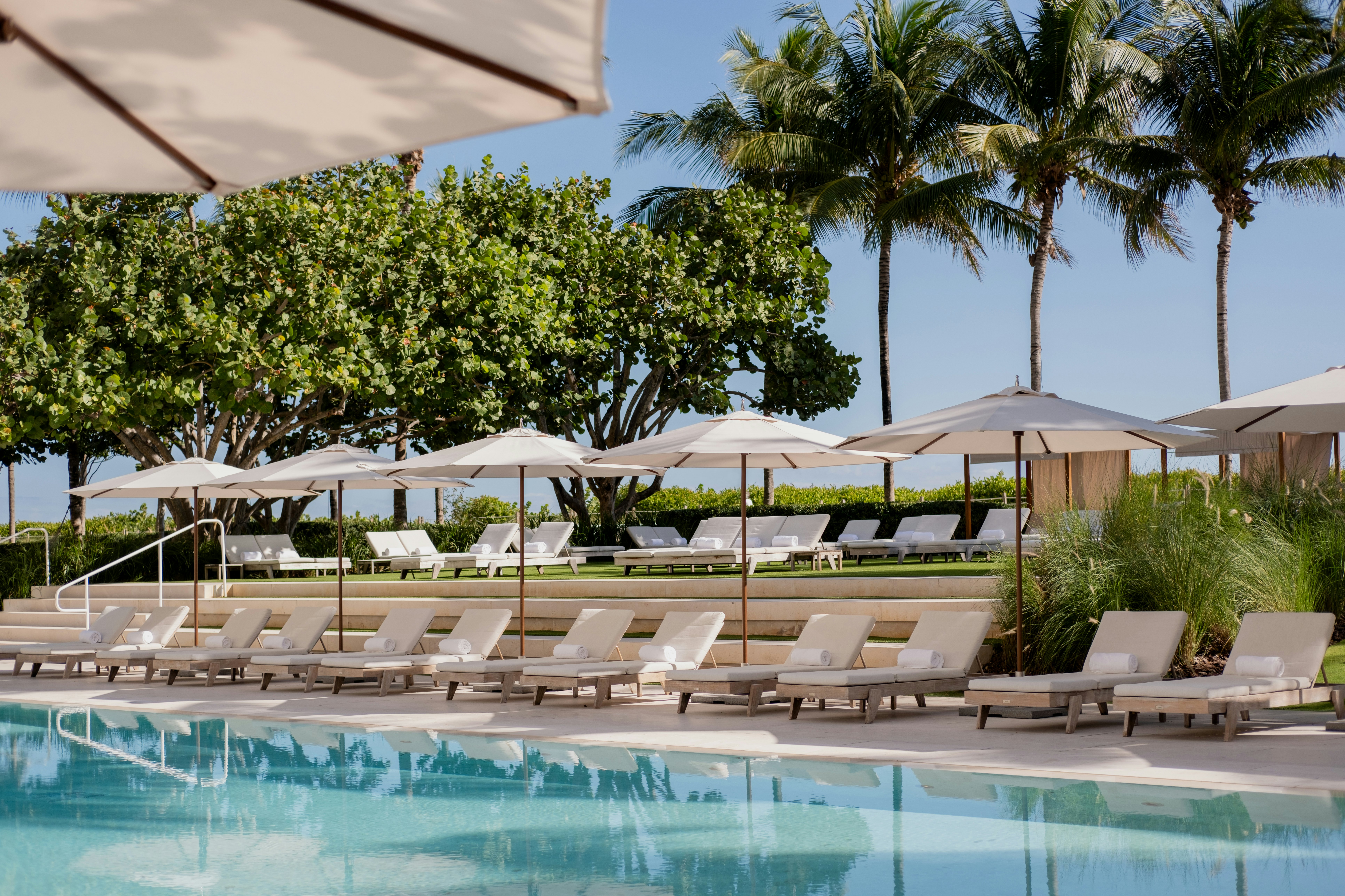 A swimming pool lined by a pristine row of cream-colored sunloungers