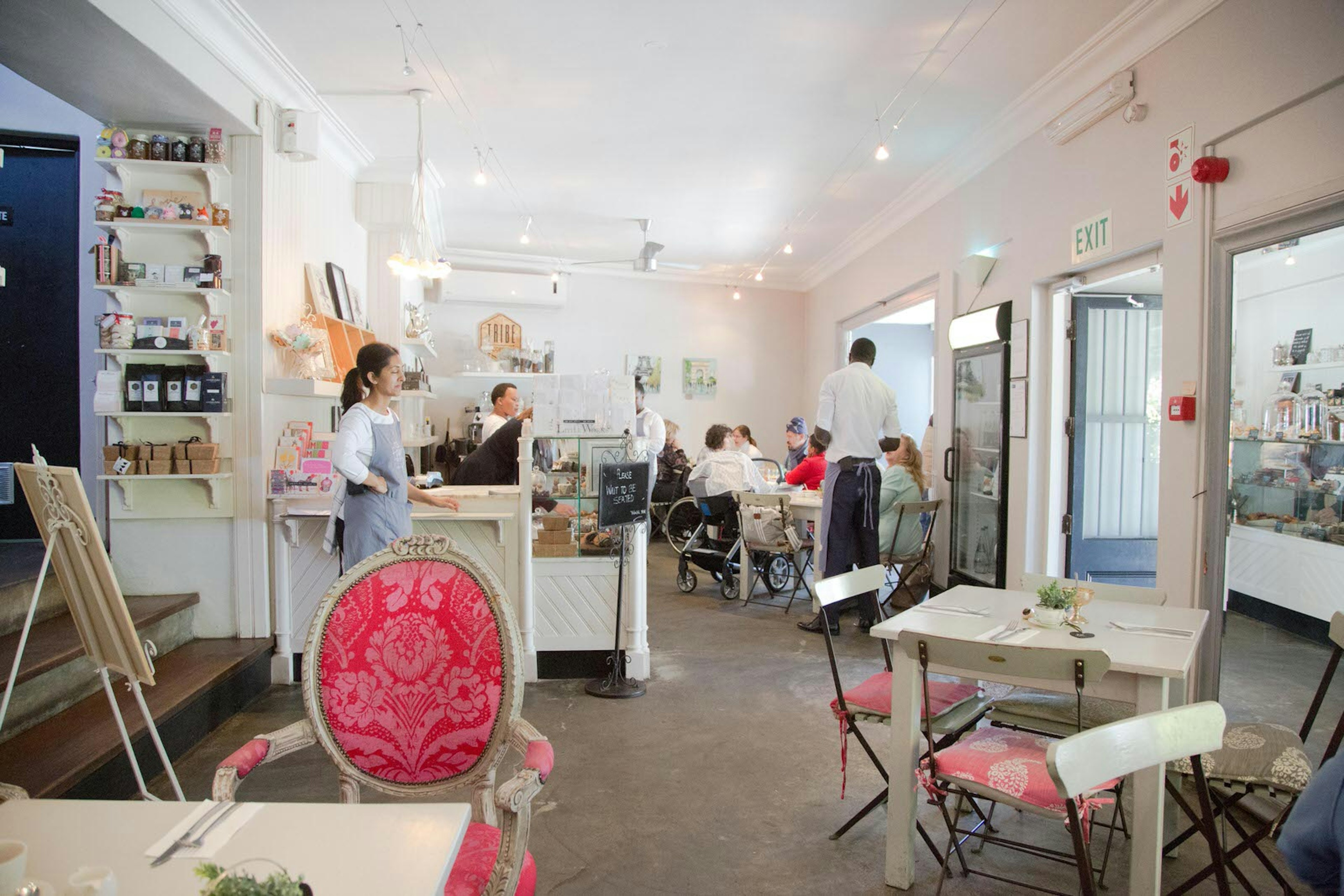 A white interior with chairs from various vintages, all sporting rich pink fabric cushion coverings; a few patrons sit at tables