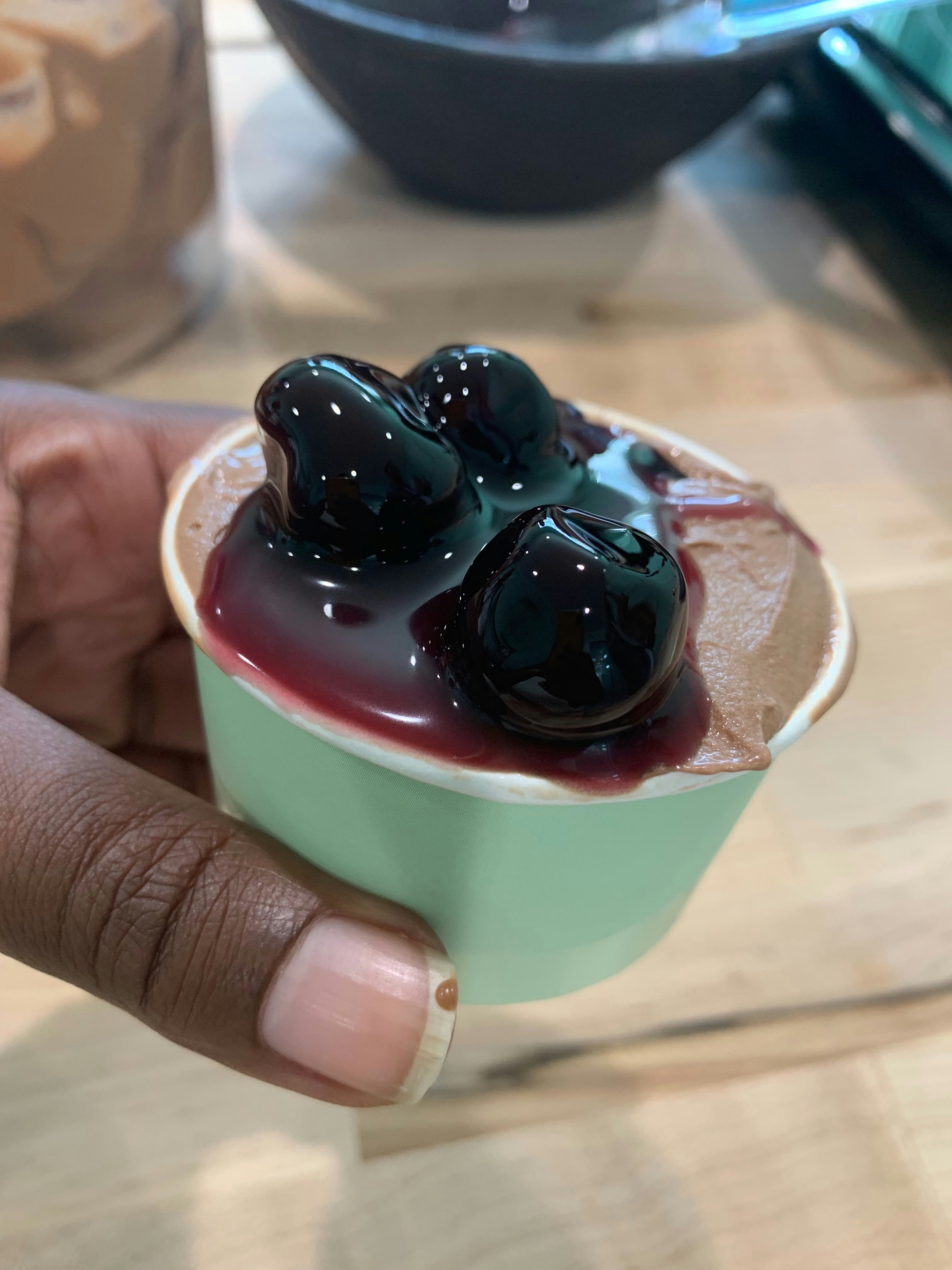 Closeup of a person holding a small cup of chocolate gelato topped with maraschino cherries