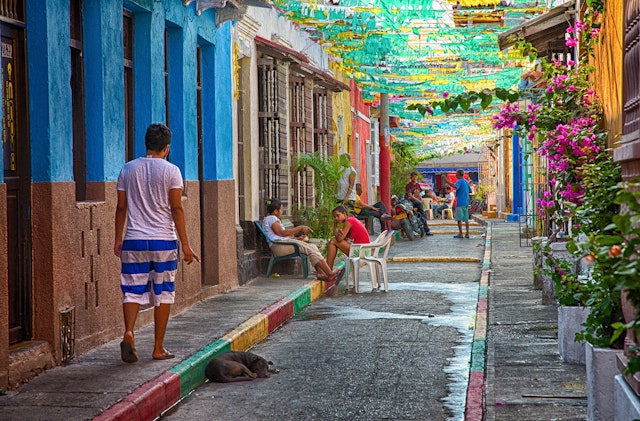 A man in white and blue striped shorts walks down a colorful street with a green and yellow paper canopy © Garytog / Getty Images