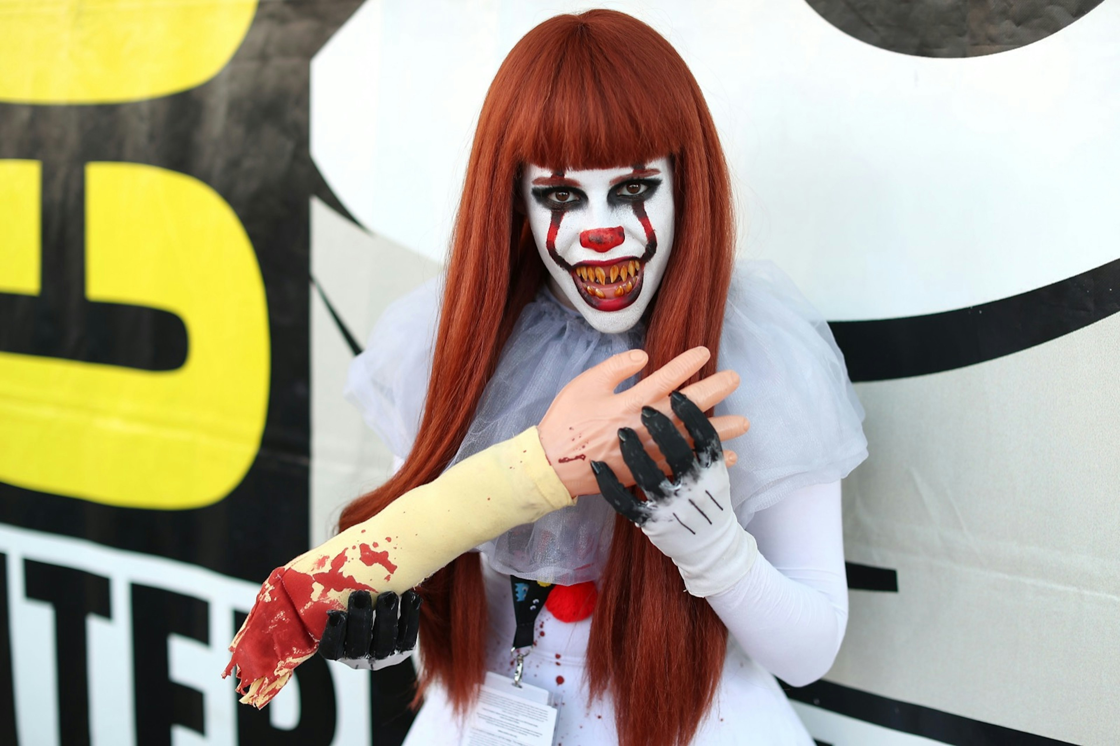 A woman dressed as an IT clown munches on a fake arm and bares her scary teeth