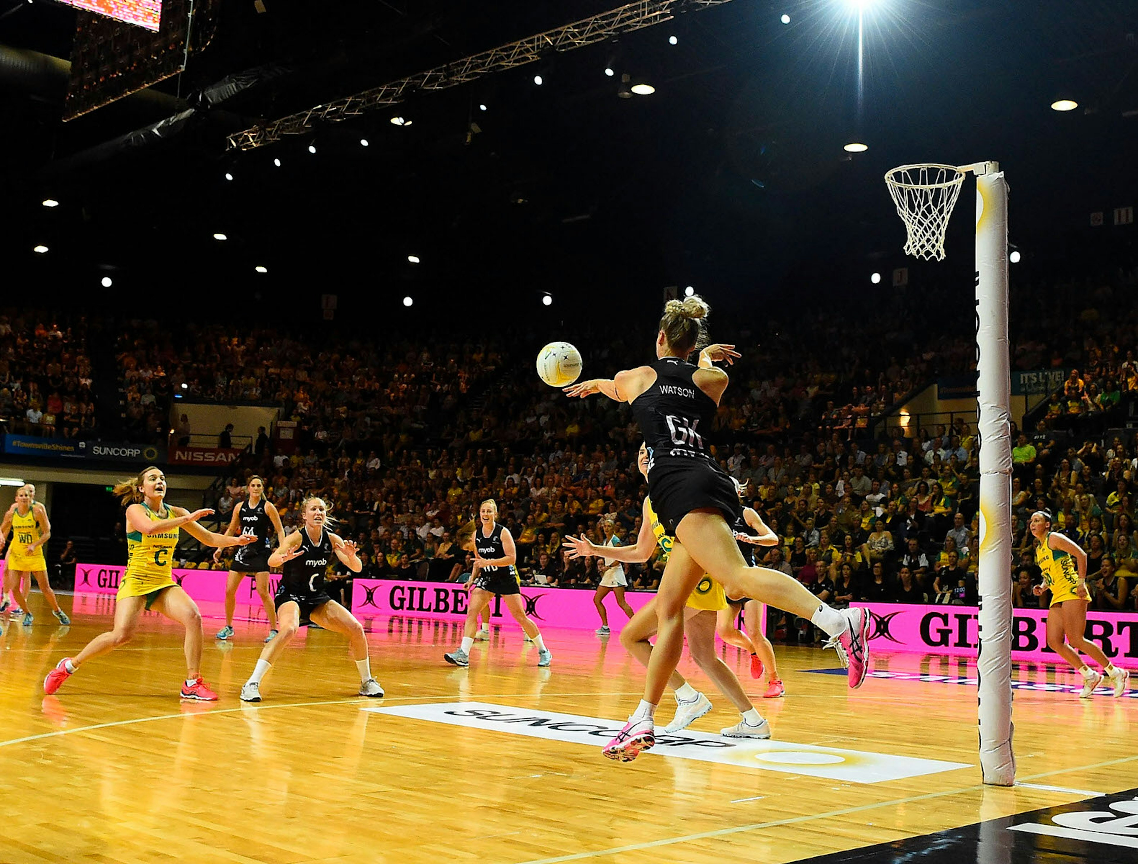 Jane Watson of the Silver Ferns desperately attempts to keep the ball in during the Constellation Cup match between the Australian Diamonds and the New Zealand Silver Ferns. In the background a large crowd fills the stadium.