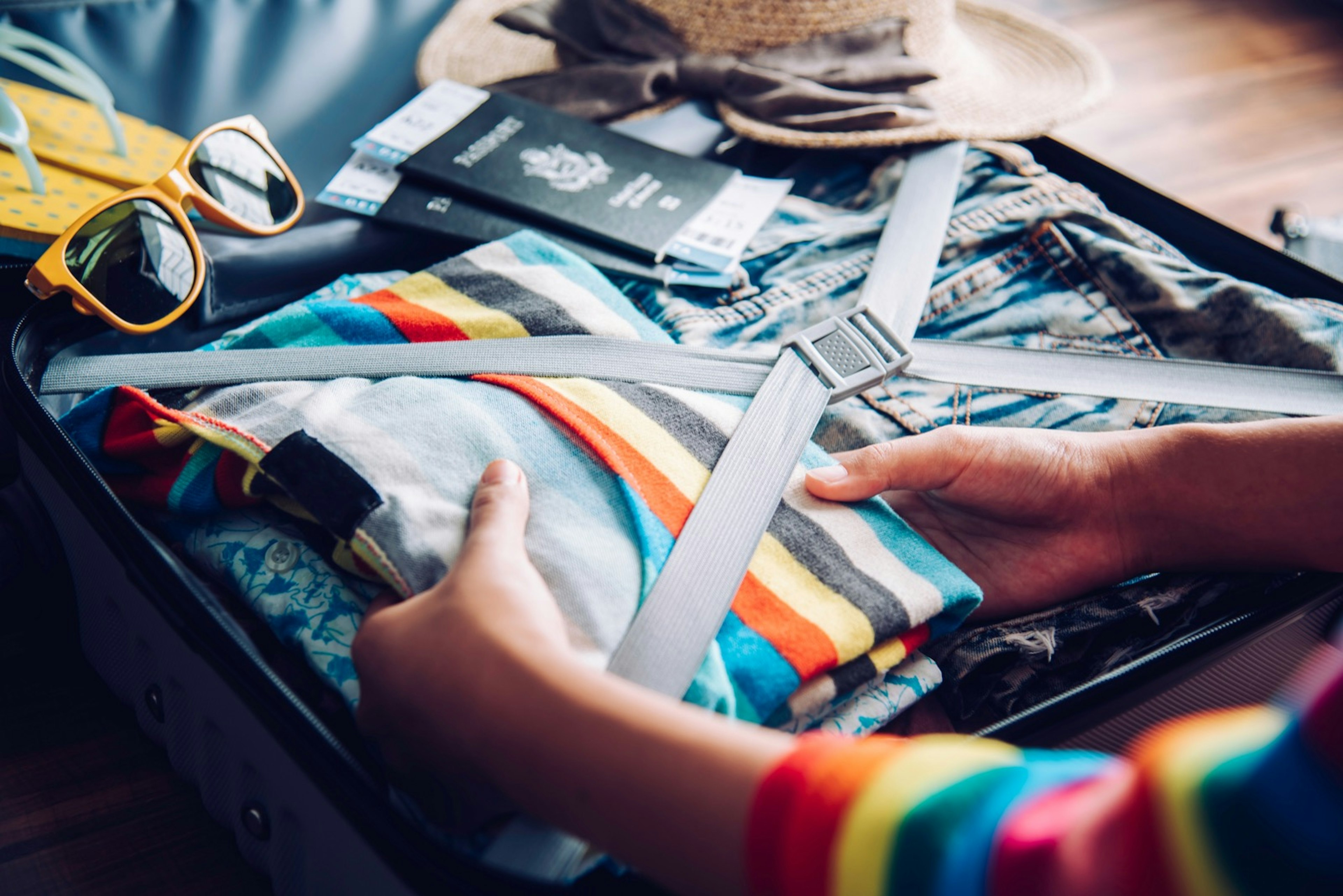 The hands of a woman are packing a colorful sweater into a suitcase at home