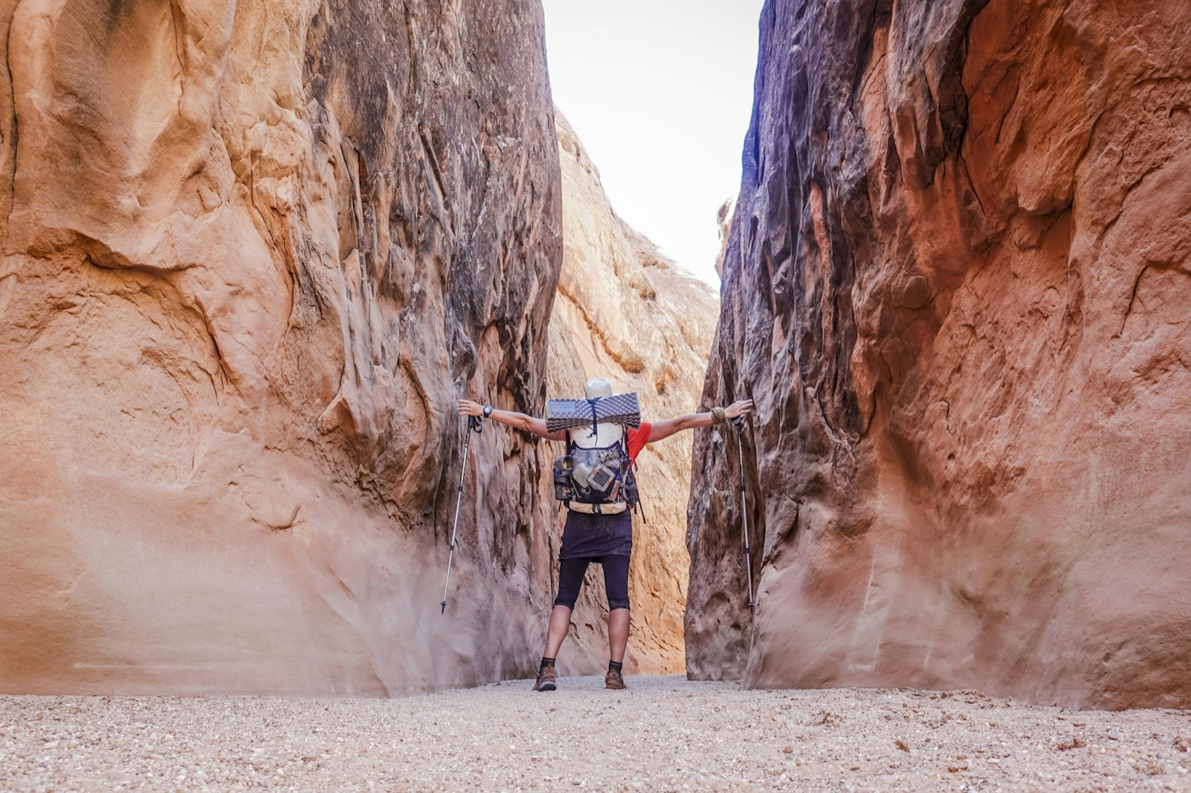 A backpacker touches both walls in a narrow canyon